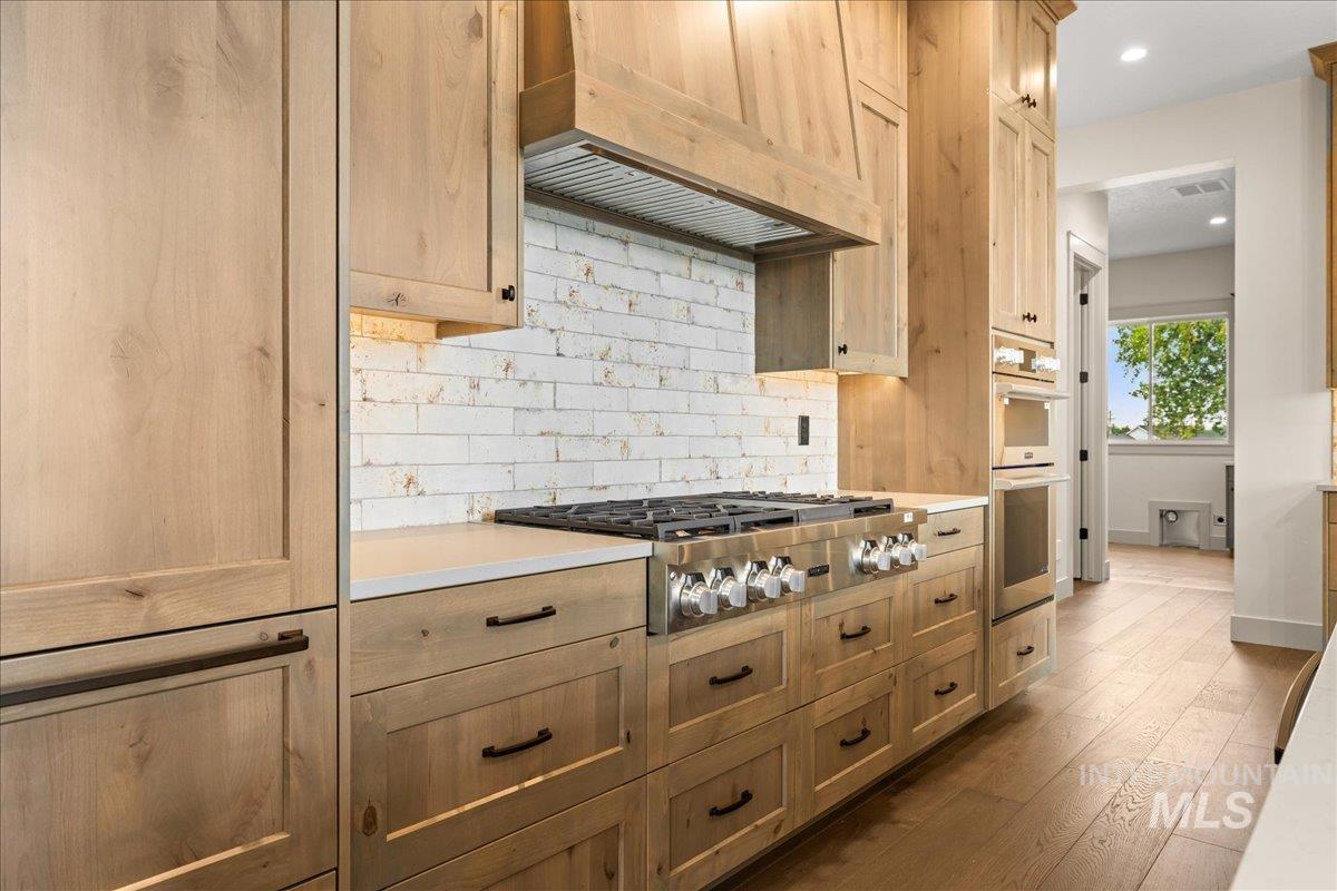 Kitchen featuring custom range hood, decorative backsplash, stainless steel appliances, dark wood-type flooring, and recessed lighting