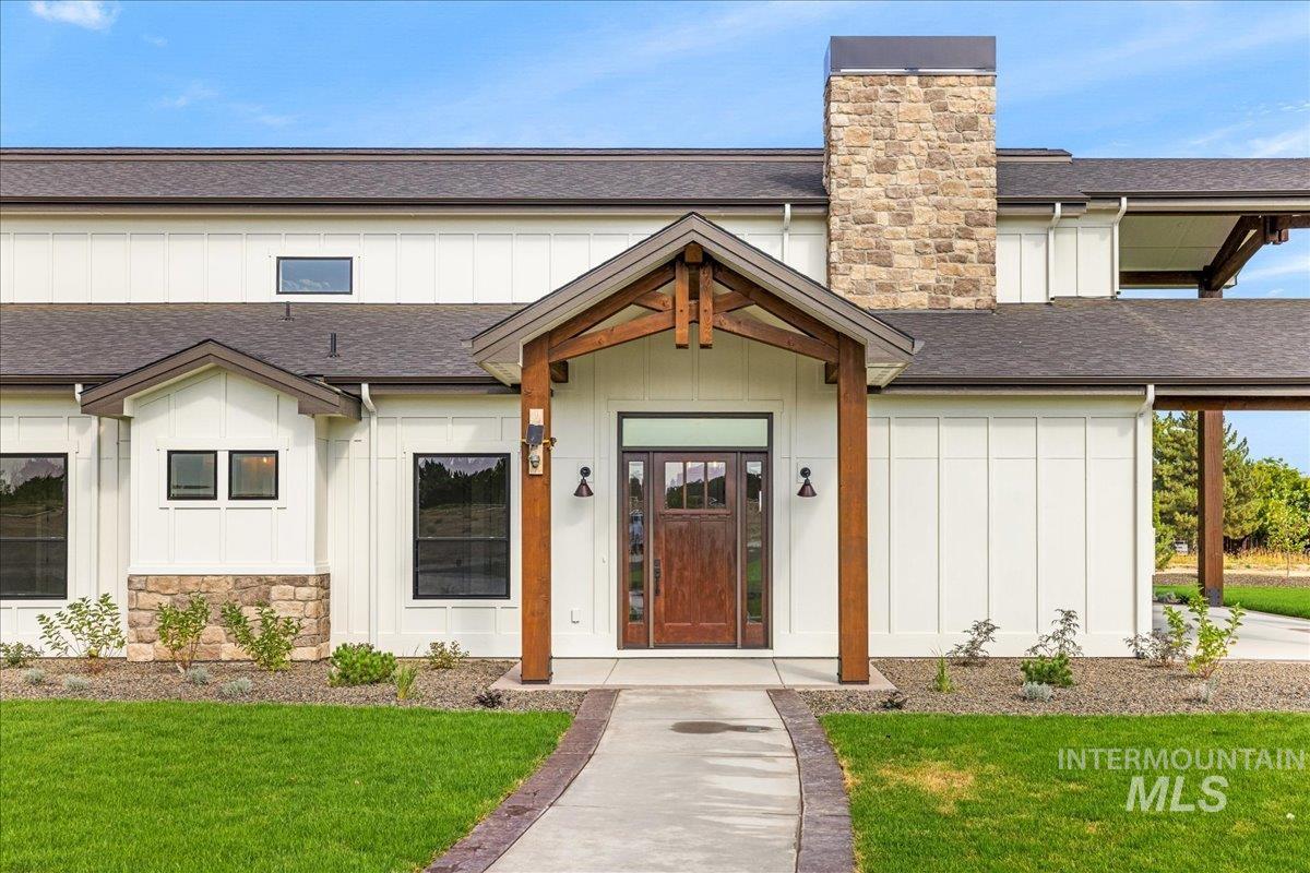 Property entrance with a shingled roof, board and batten siding, a lawn, and a chimney