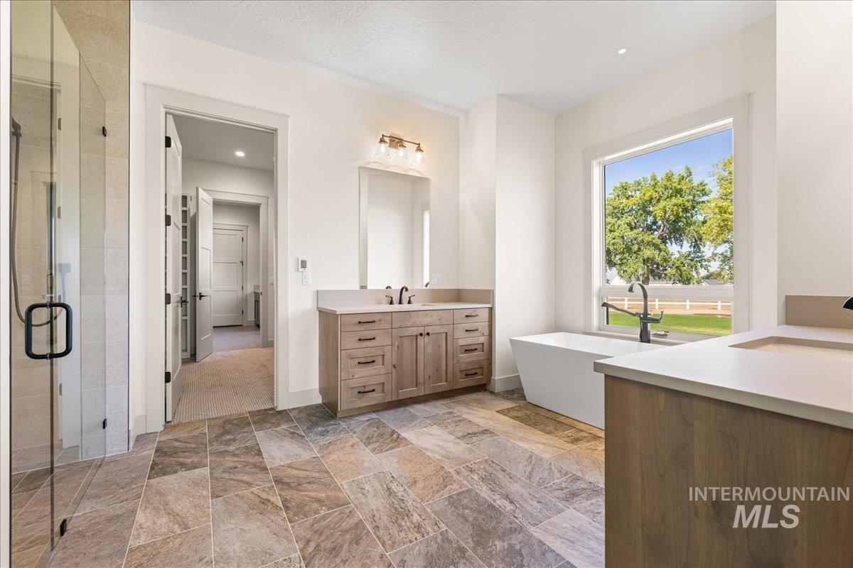 Bathroom featuring a shower stall, vanity, a soaking tub, light stone finish flooring, and recessed lighting