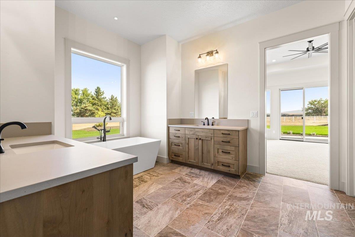 Bathroom with two vanities, a soaking tub, light stone finish flooring, and plenty of natural light