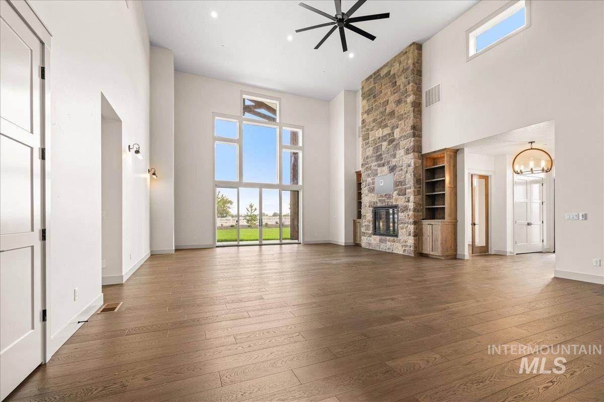 Unfurnished living room featuring a stone fireplace, a high ceiling, hardwood / wood-style flooring, ceiling fan, and a chandelier