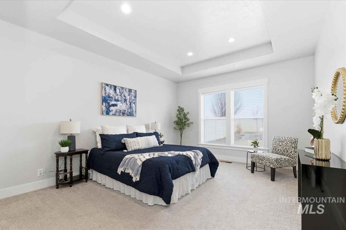Bedroom with light carpet, recessed lighting, and a tray ceiling