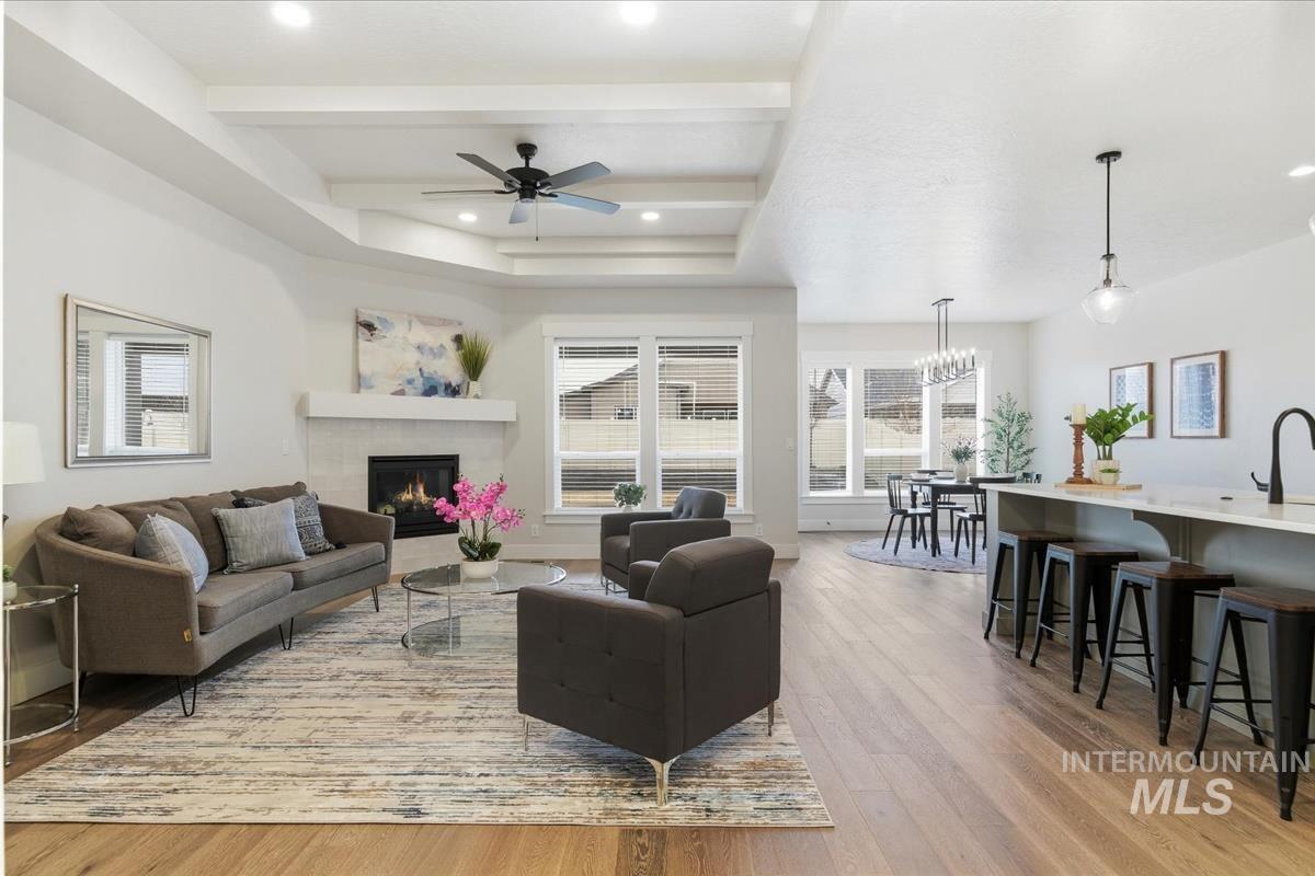 Living area with a ceiling fan, a tile fireplace, light wood-style flooring, recessed lighting, and a raised ceiling