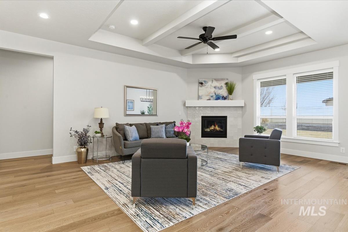 Living area with ceiling fan, light wood-style flooring, a tray ceiling, a fireplace, and recessed lighting