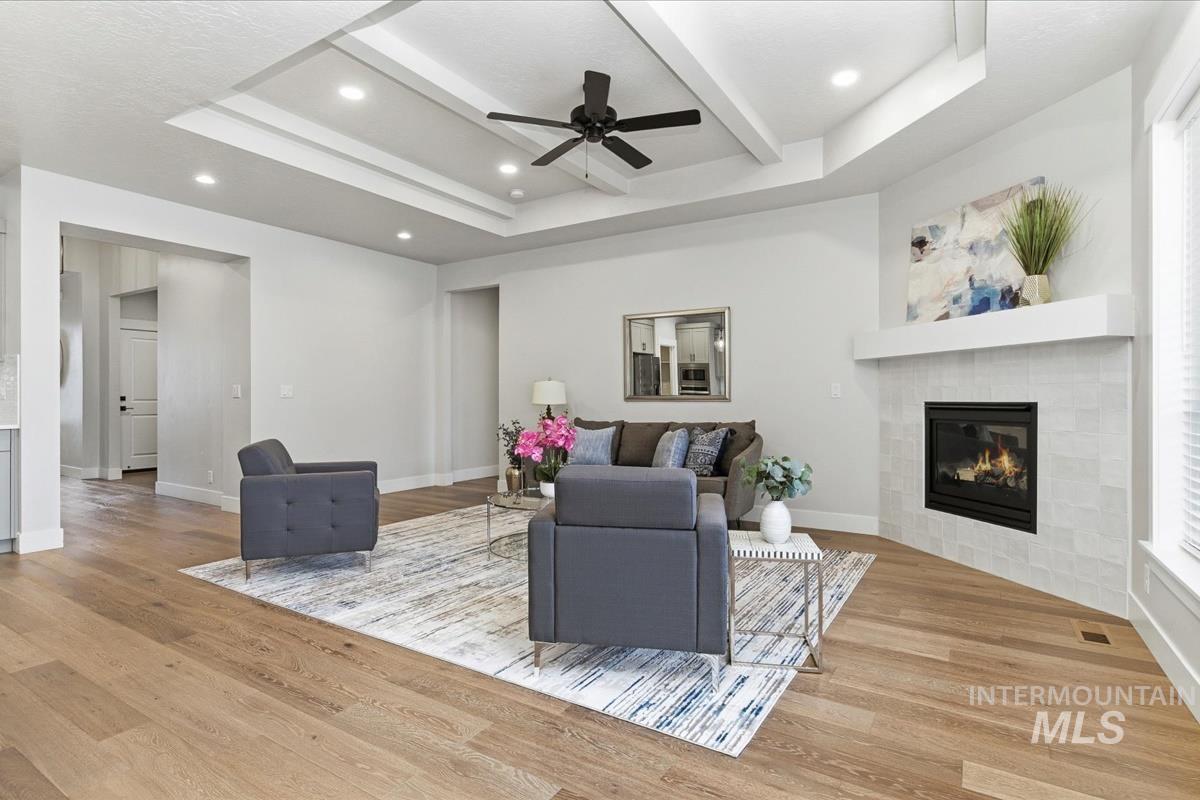 Living area with a ceiling fan, light wood-style flooring, a fireplace, a raised ceiling, and recessed lighting