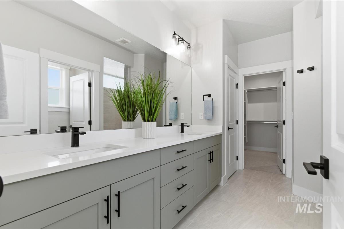 Full bathroom with double vanity, a walk in closet, and light tile patterned floors