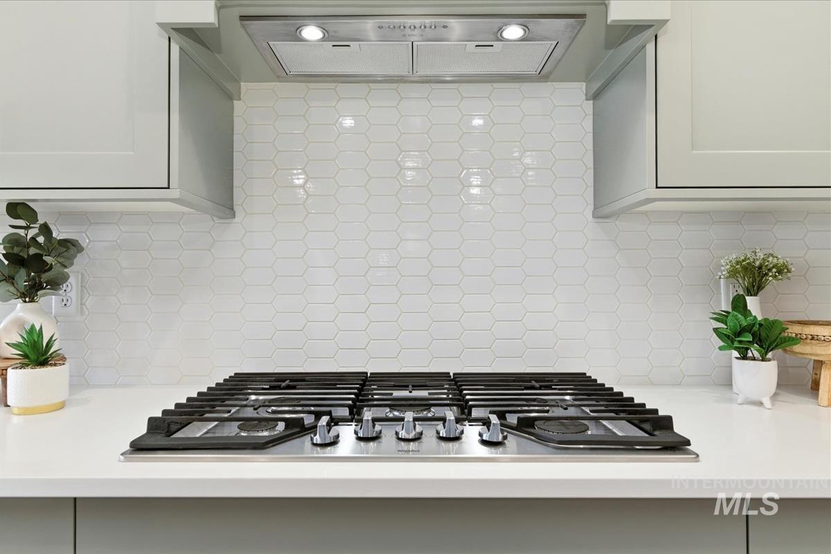 Kitchen view of extractor fan, stainless steel gas stovetop, and decorative backsplash