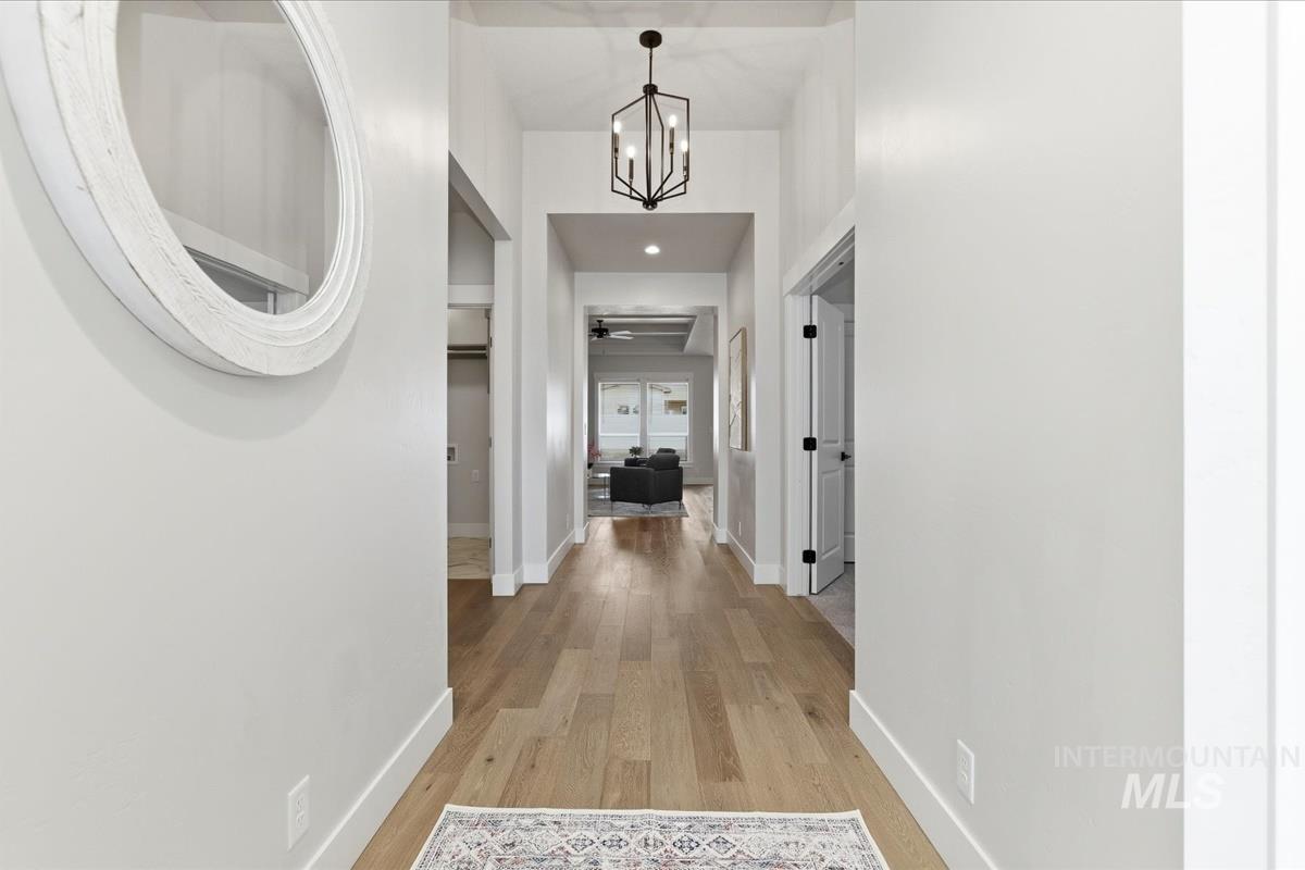 Hallway featuring hanging lights, light wood-type flooring, and a high ceiling