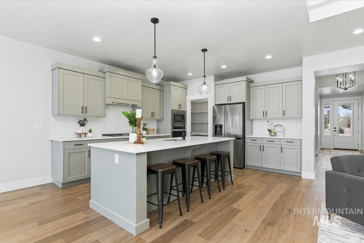 Kitchen with a kitchen breakfast bar, gray cabinets, stainless steel appliances, an island with sink, and light wood finished floors