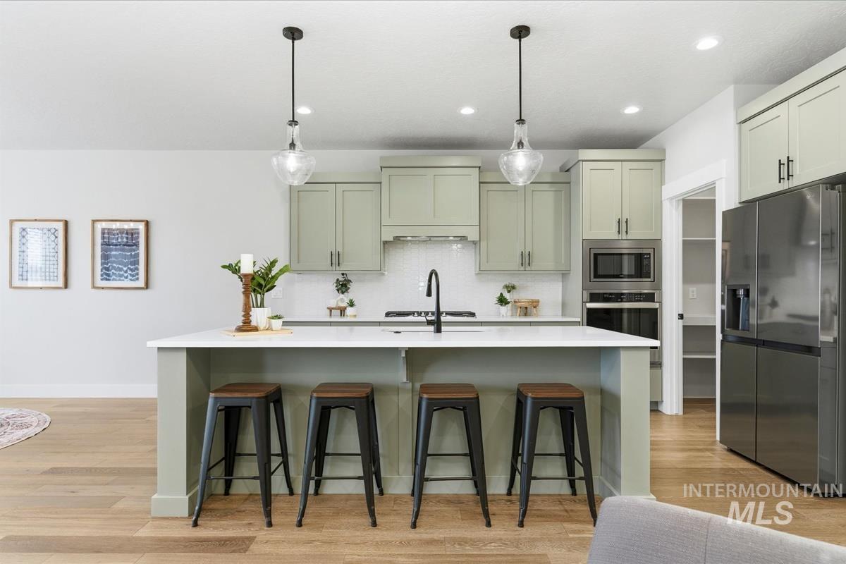 Kitchen featuring stainless steel appliances, decorative light fixtures, a breakfast bar, a kitchen island with sink, and light wood-style floors