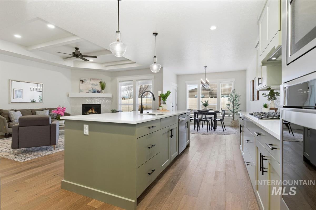 Kitchen with pendant lighting, stainless steel appliances, light wood-style floors, a warm lit fireplace, and ceiling fan