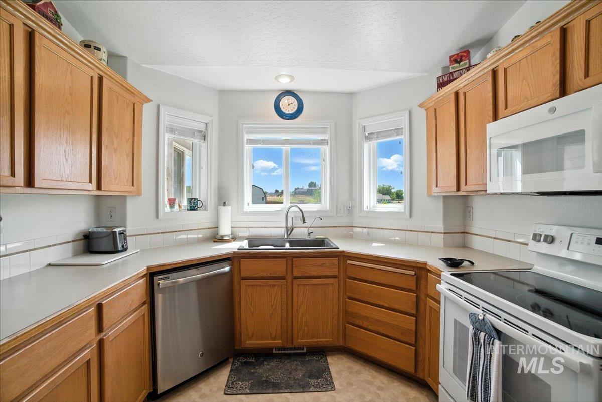 Kitchen with white appliances, light countertops, a textured ceiling, and brown cabinets