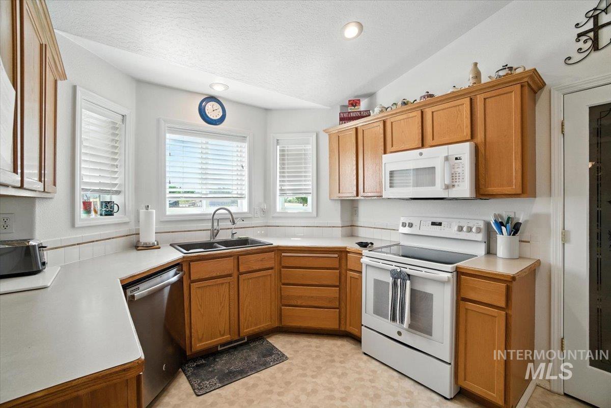 Kitchen featuring white appliances, light countertops, a textured ceiling, brown cabinetry, and light floors