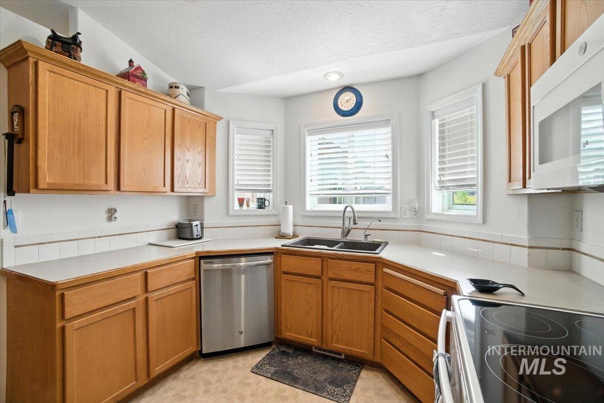 Kitchen featuring white appliances, a textured ceiling, light countertops, and brown cabinets
