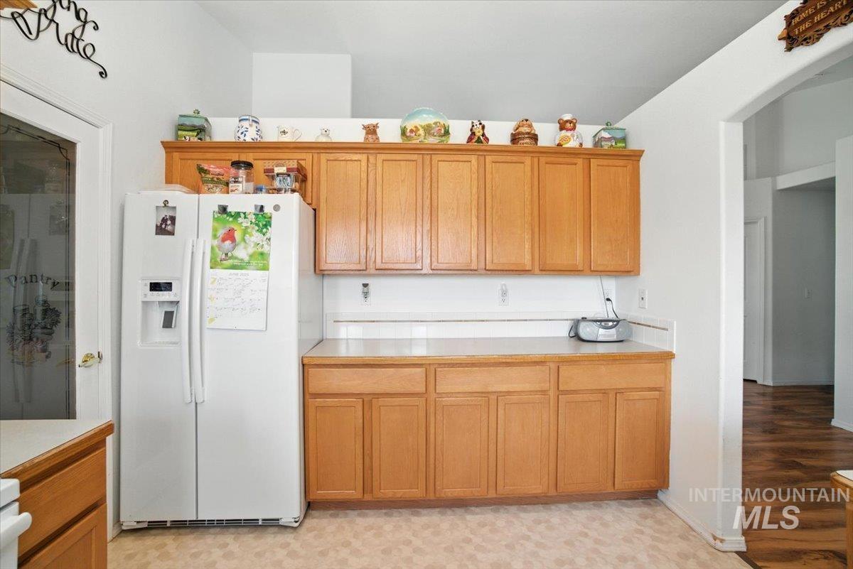 Kitchen featuring white fridge with ice dispenser, light countertops, arched walkways, and brown cabinetry