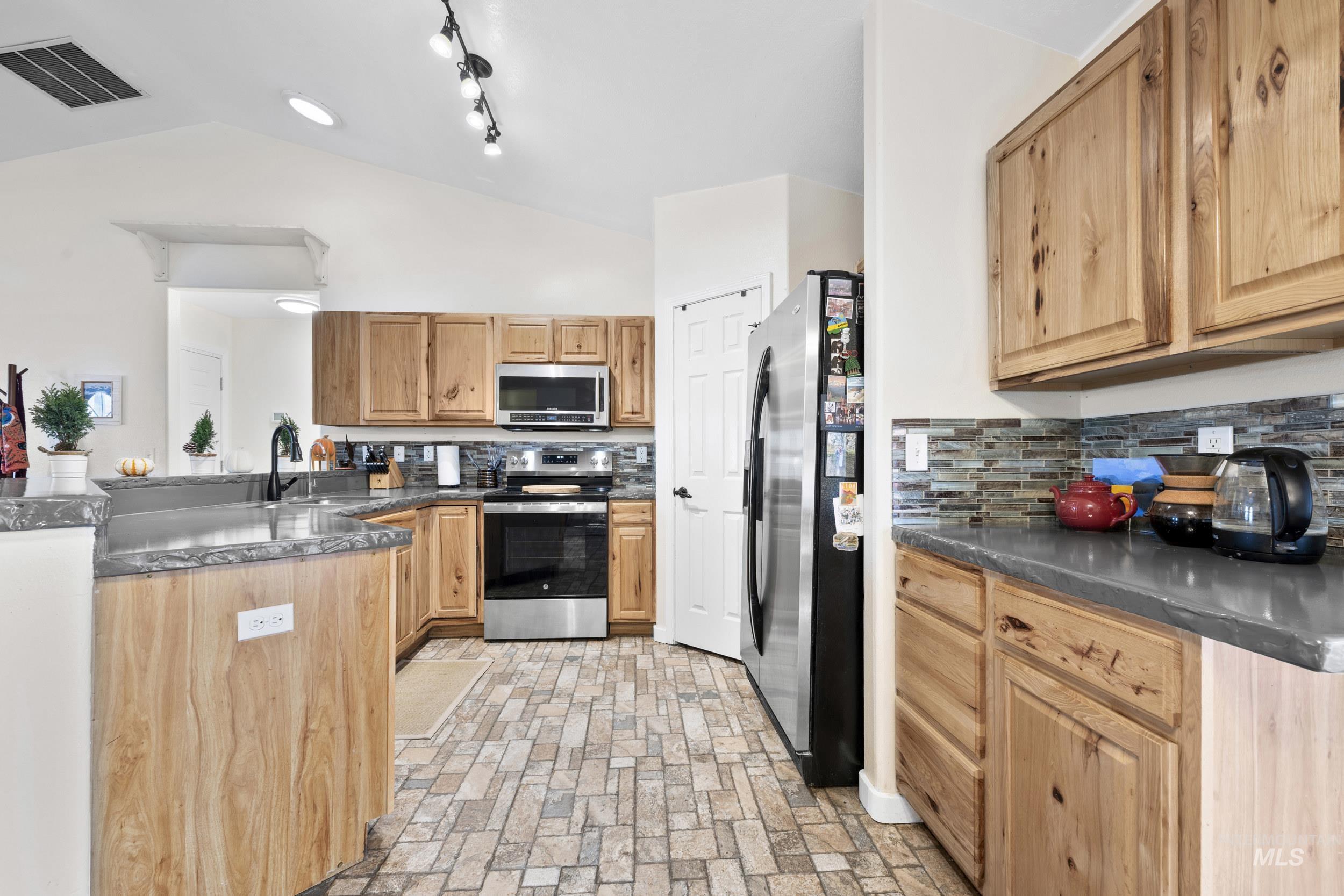 Kitchen featuring stainless steel appliances, vaulted ceiling, a peninsula, brick patterned floors, and backsplash