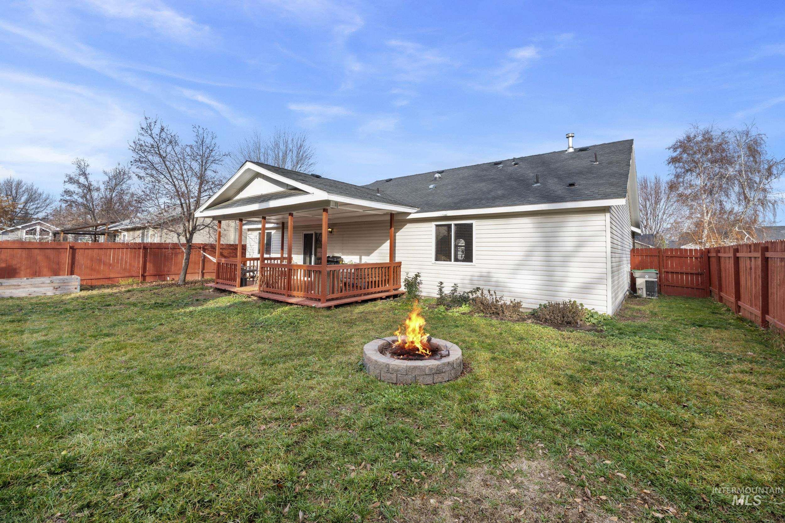 Rear view of house featuring a fenced backyard, an outdoor fire pit, a deck, and a shingled roof