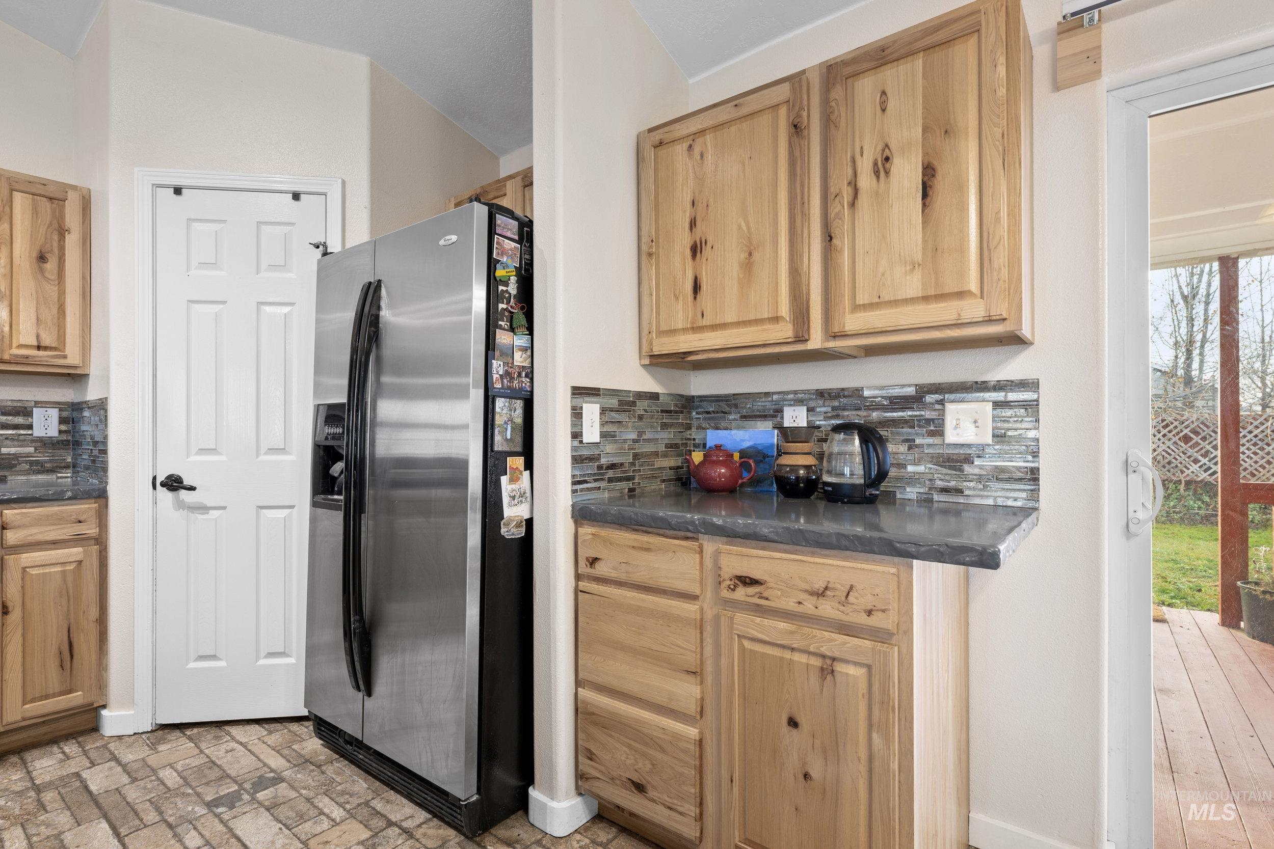 Kitchen featuring stainless steel fridge, tasteful backsplash, dark stone counters, and brick patterned flooring