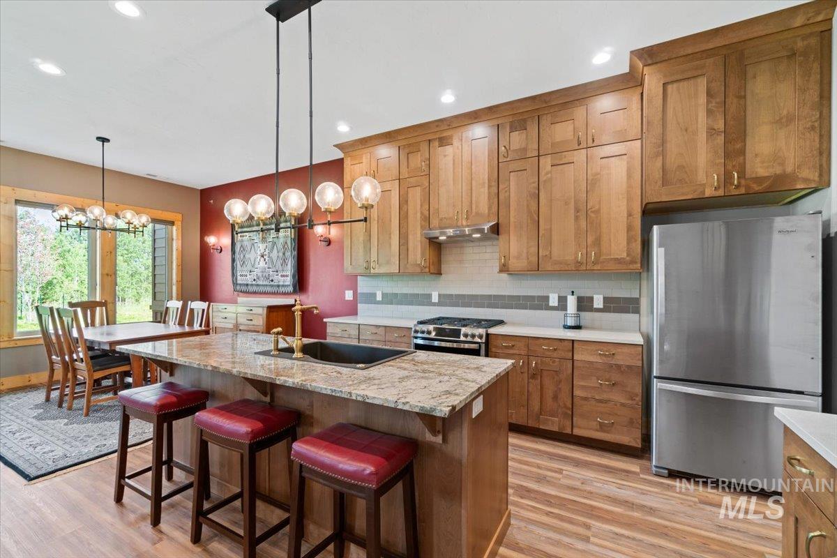 Kitchen featuring stainless steel appliances, light wood-style floors, a chandelier, brown cabinetry, and recessed lighting