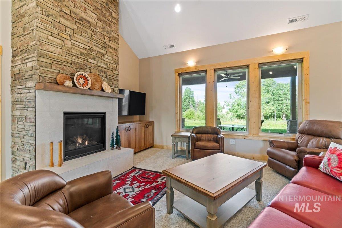 Living area featuring light carpet, a stone fireplace, and high vaulted ceiling