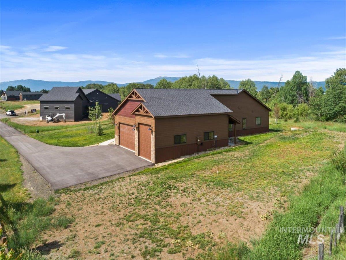 View of side of property featuring a mountain view, a yard, a shingled roof, and a garage