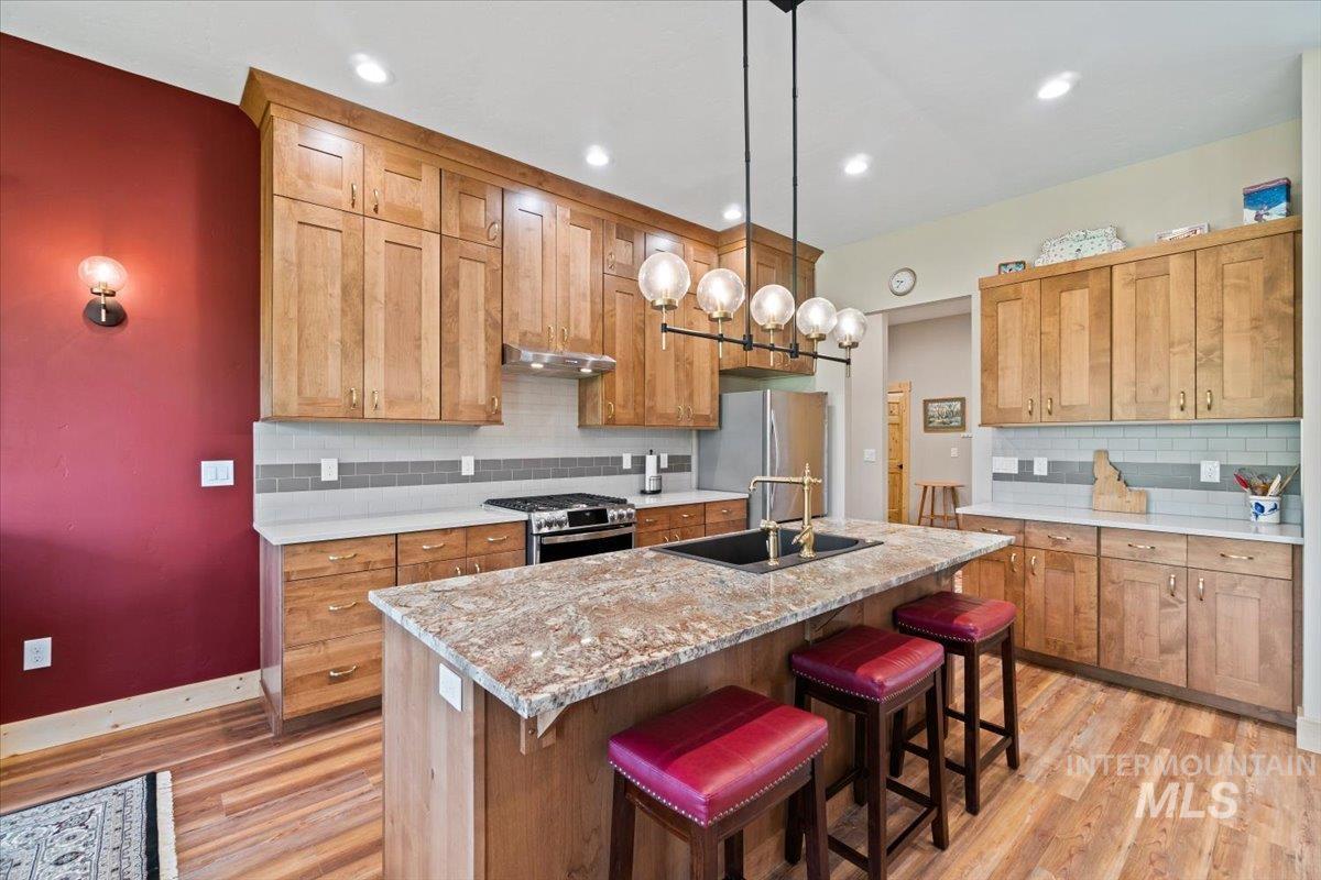 Kitchen featuring appliances with stainless steel finishes, light wood-style floors, decorative backsplash, a center island with sink, and recessed lighting