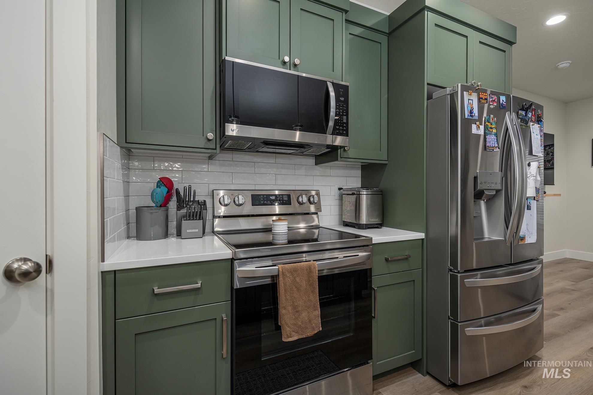 Kitchen with green cabinets, stainless steel appliances, light wood-type flooring, backsplash, and recessed lighting