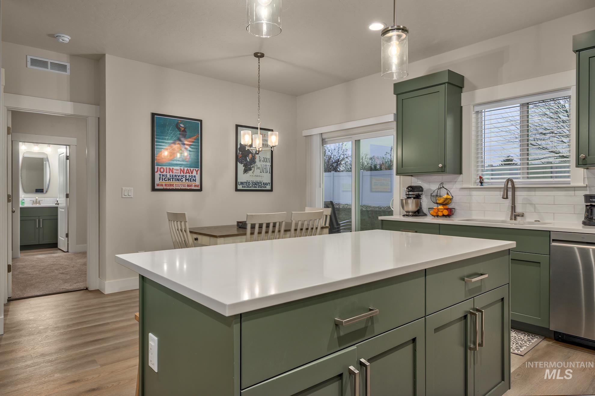 Kitchen with green cabinetry, backsplash, pendant lighting, and light wood-style flooring
