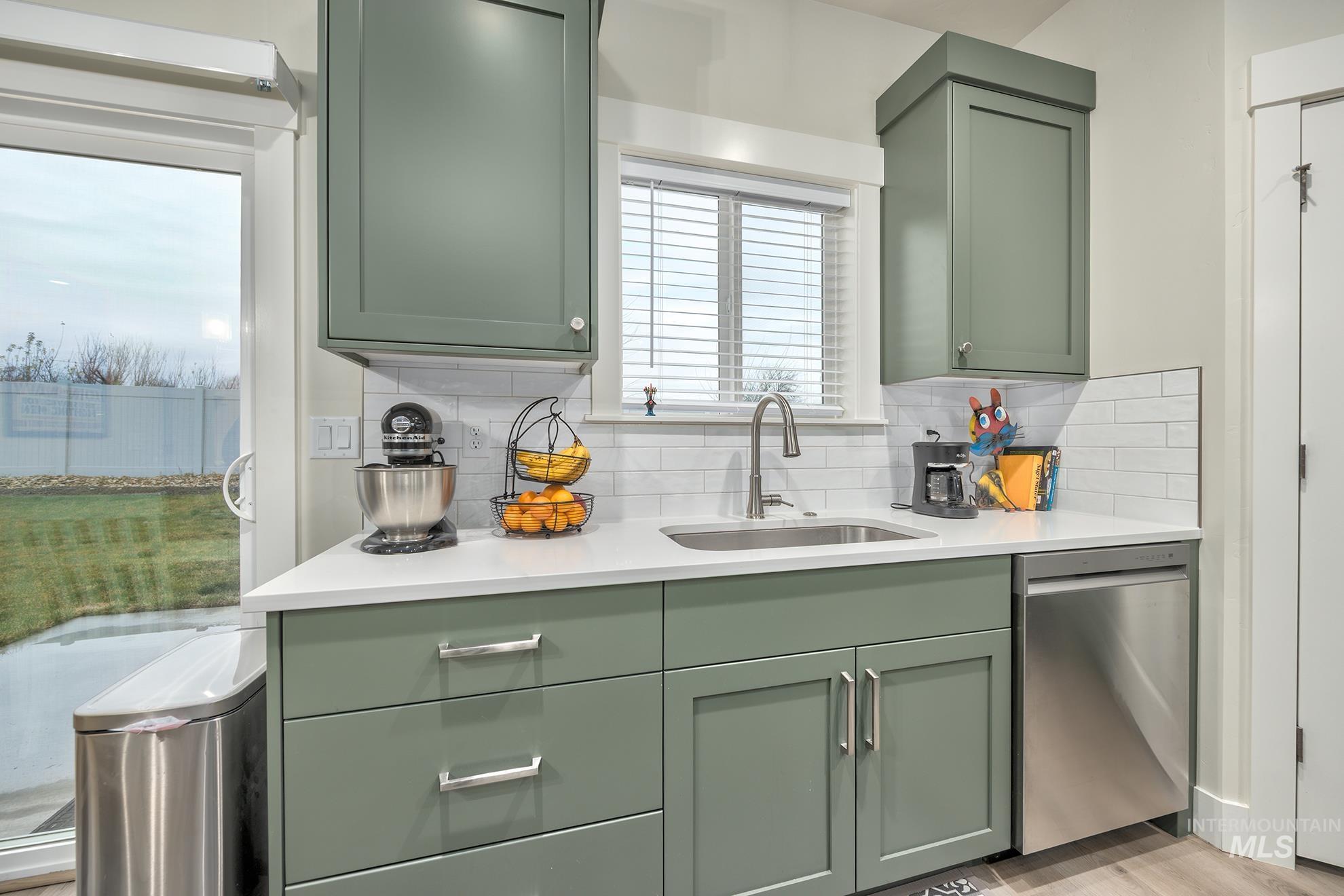 Kitchen featuring green cabinets, stainless steel dishwasher, and backsplash