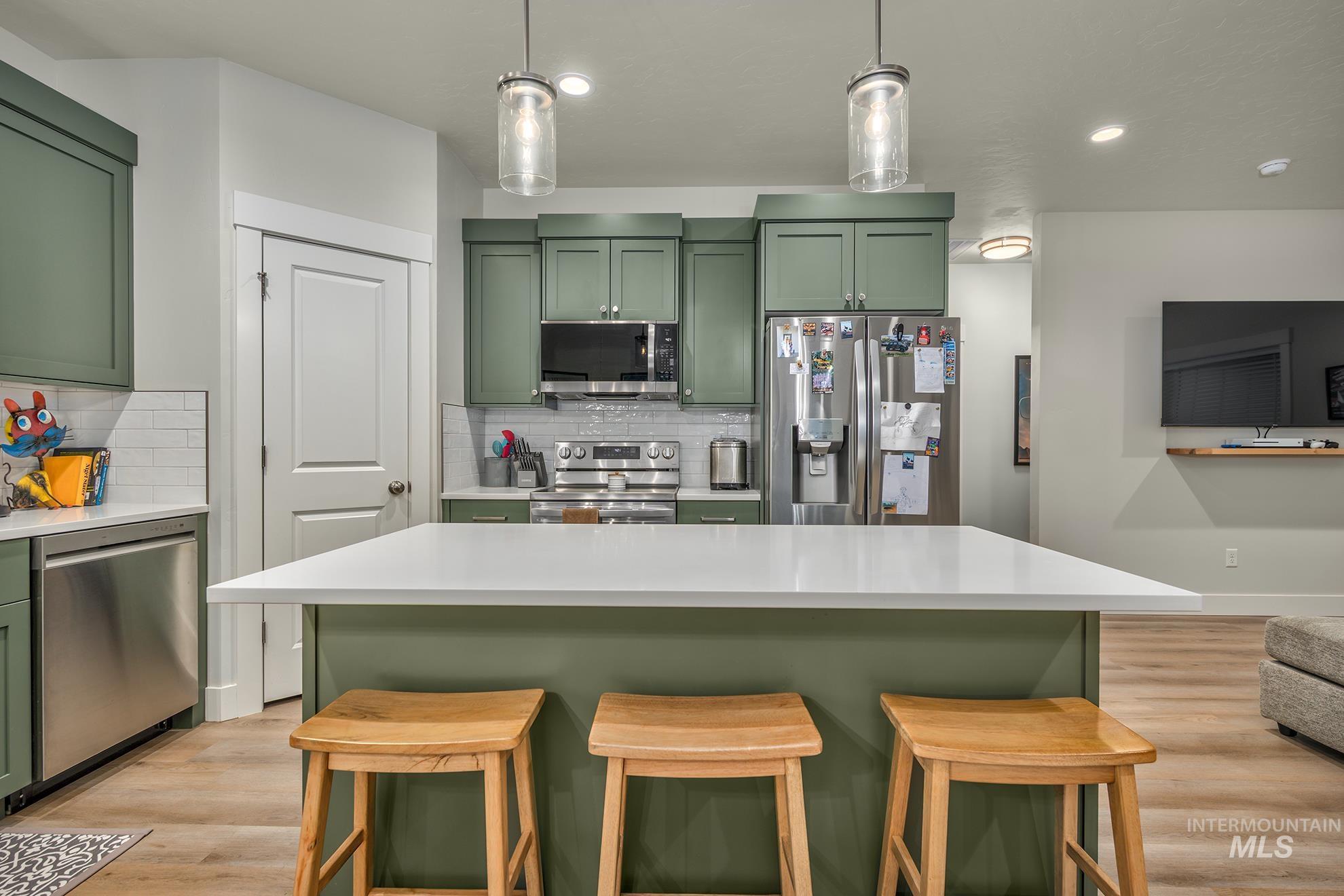 Kitchen with green cabinetry, stainless steel appliances, a kitchen breakfast bar, a kitchen island, and light wood-style flooring