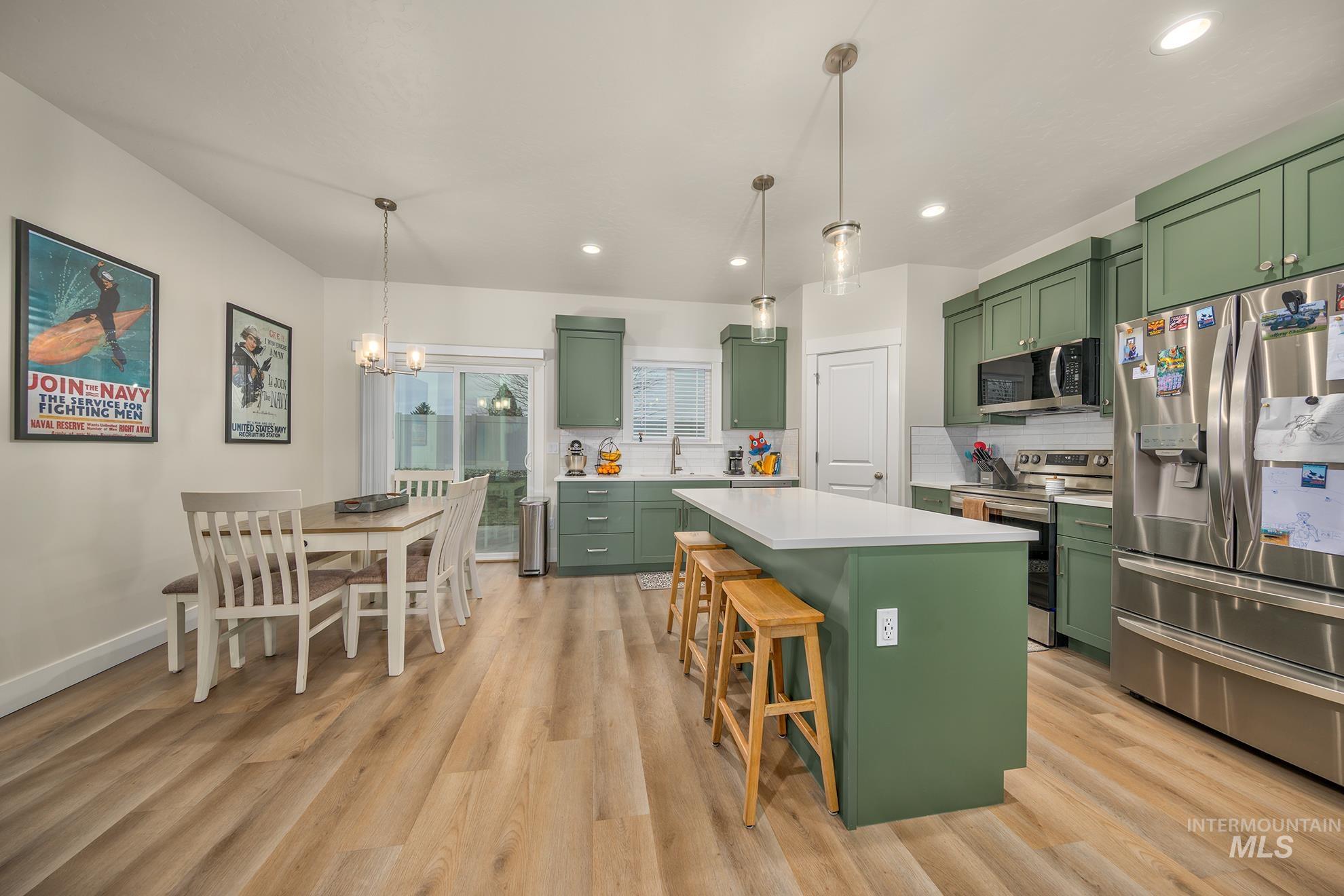 Kitchen with green cabinets, appliances with stainless steel finishes, pendant lighting, a kitchen island, and a breakfast bar area