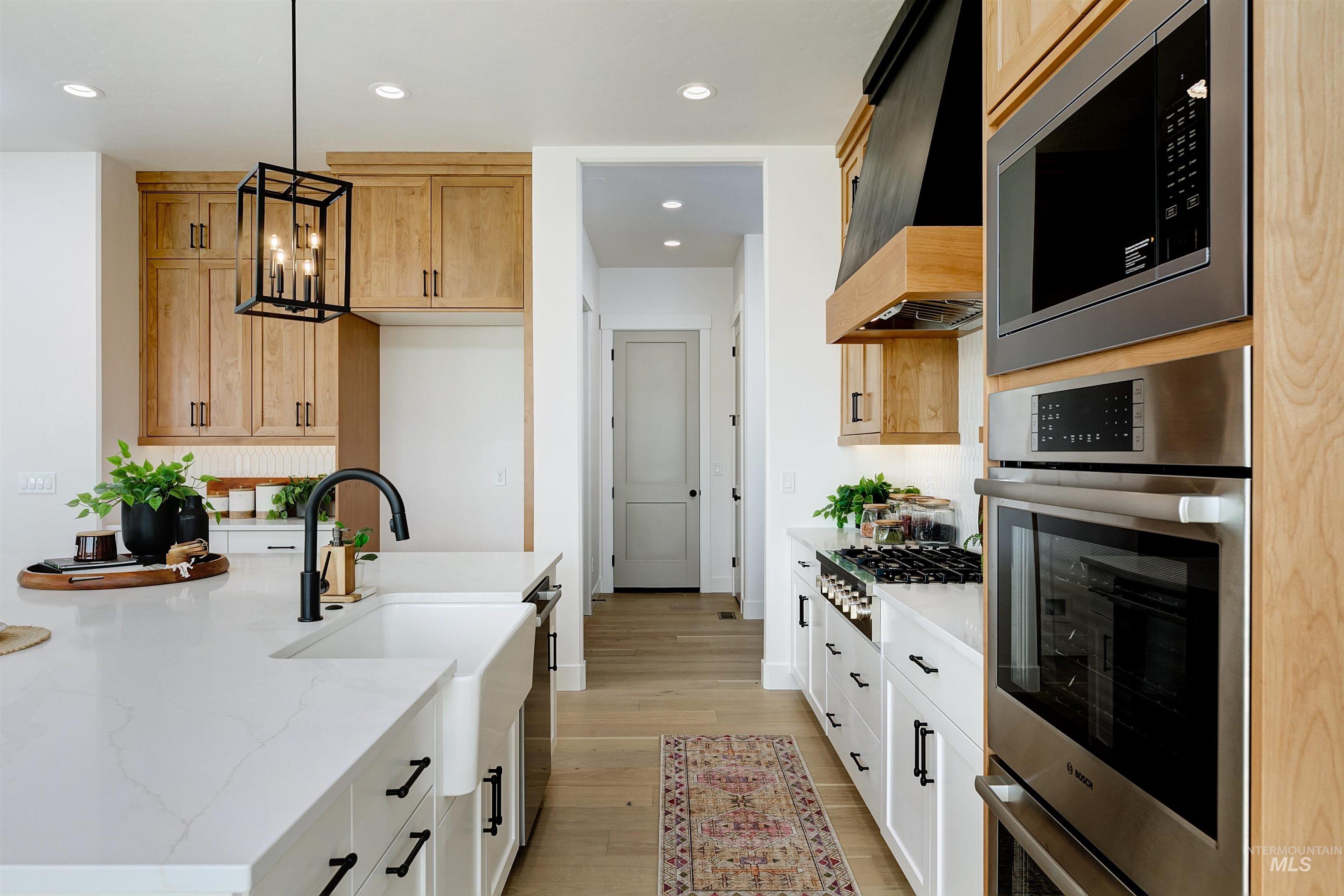 Kitchen featuring stainless steel appliances, light stone countertops, light wood-style flooring, a center island with sink, and suspended lighting