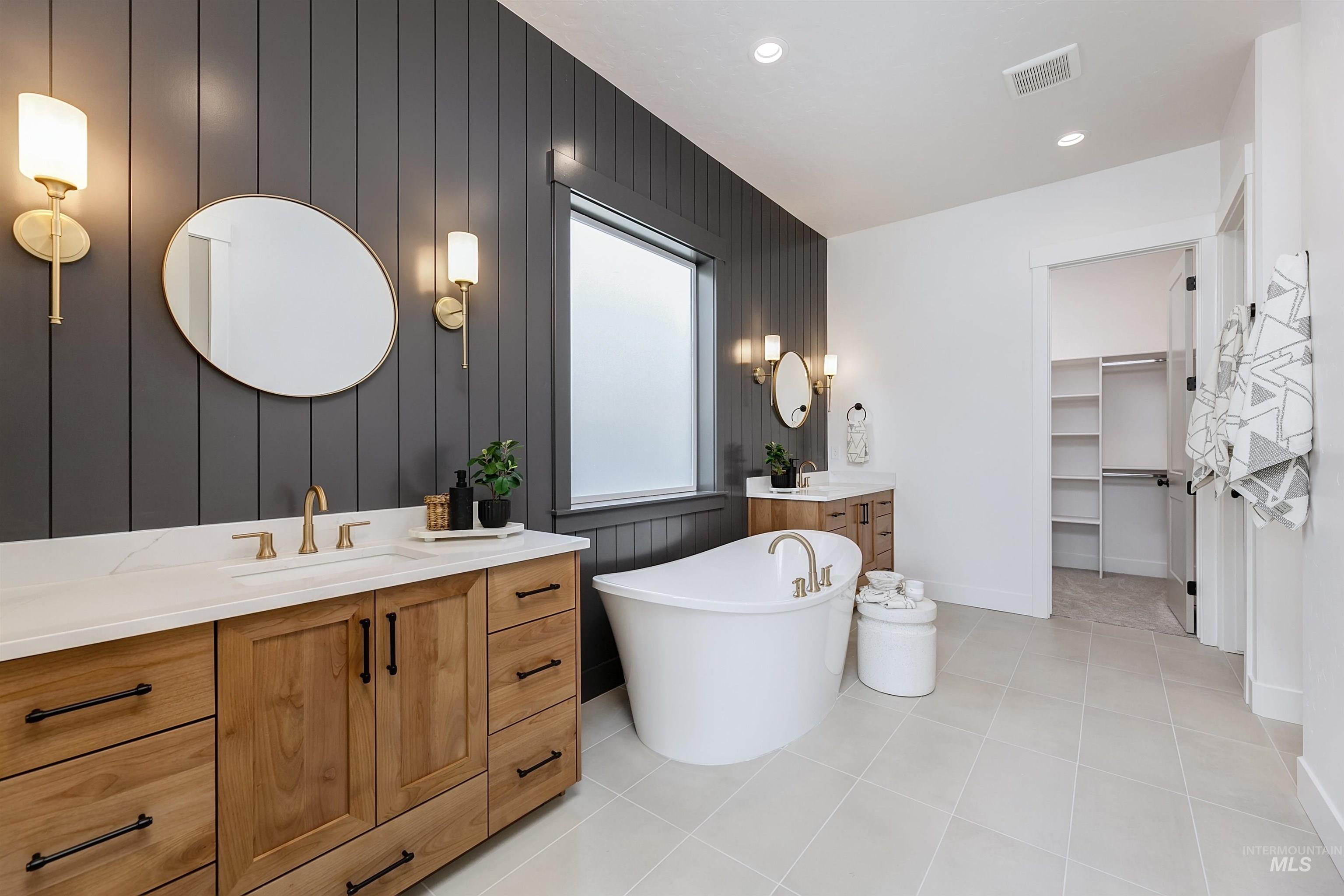 Bathroom with two vanities, a spacious closet, an accent wall, a soaking tub, and recessed lighting