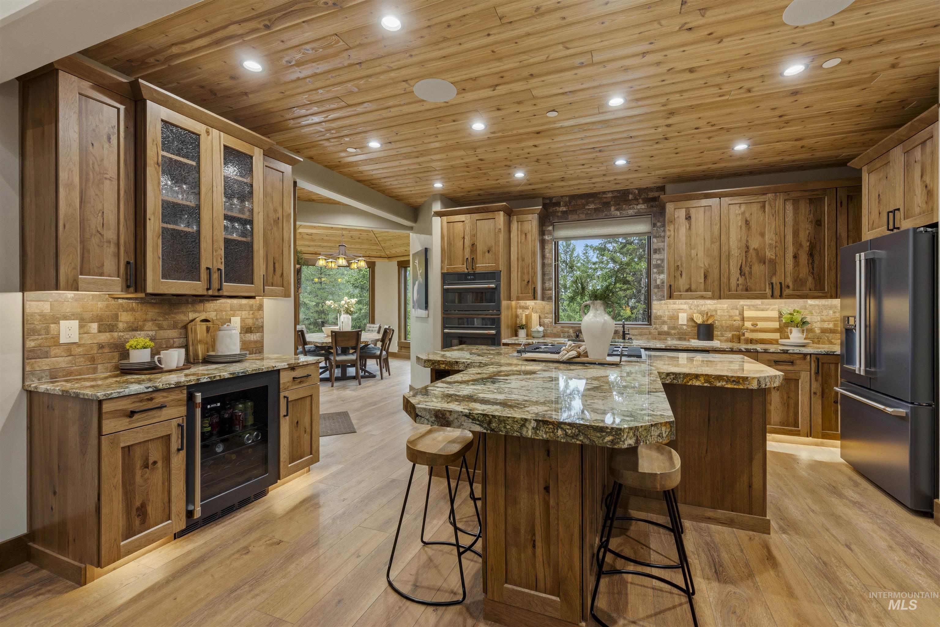 Gourmet kitchen featuring wood-finish flooring, a wood-paneled ceiling with recessed lighting, custom wood cabinetry, granite countertops, and a built-in beverage refrigerator