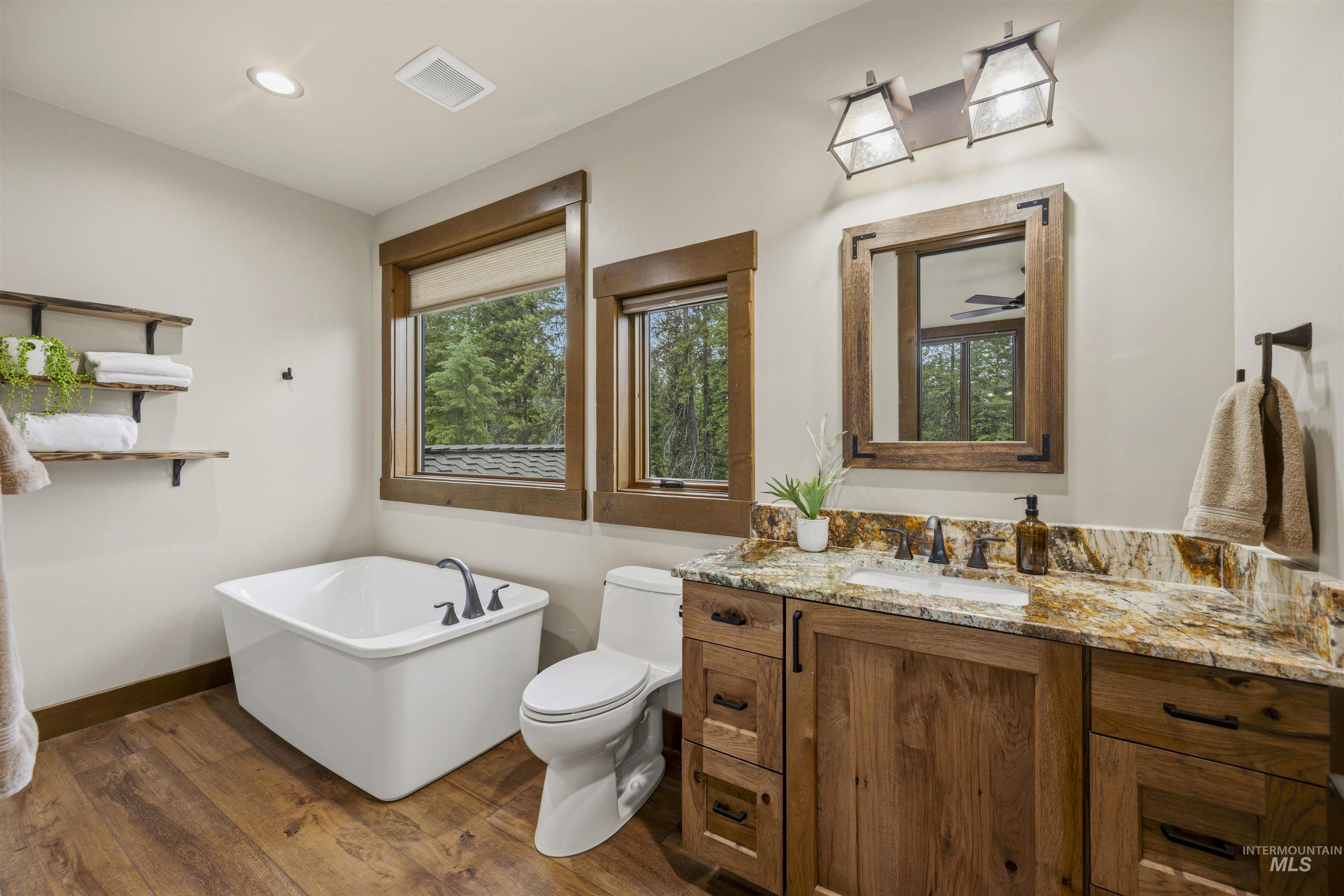 Bathroom featuring a freestanding soaking tub with dark bronze fixtures, a wood-finish vanity with a stone countertop, a framed mirror, and wood-finish flooring - Ensuite to Bedroom 5