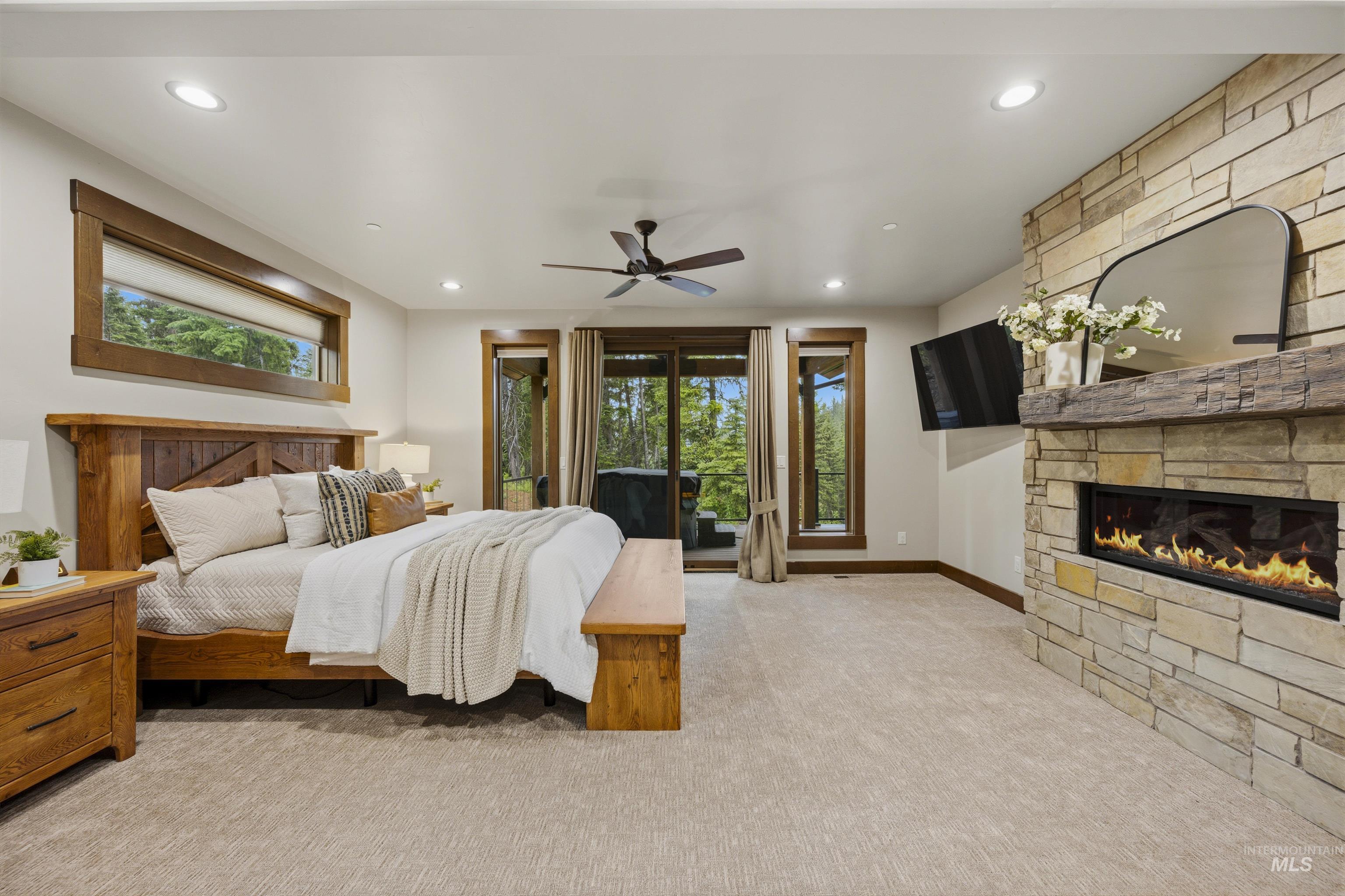 Spacious room featuring a stone-clad fireplace with a natural wood mantle, a ceiling fan, recessed lighting, and direct access to an exterior space - Primary Main Level