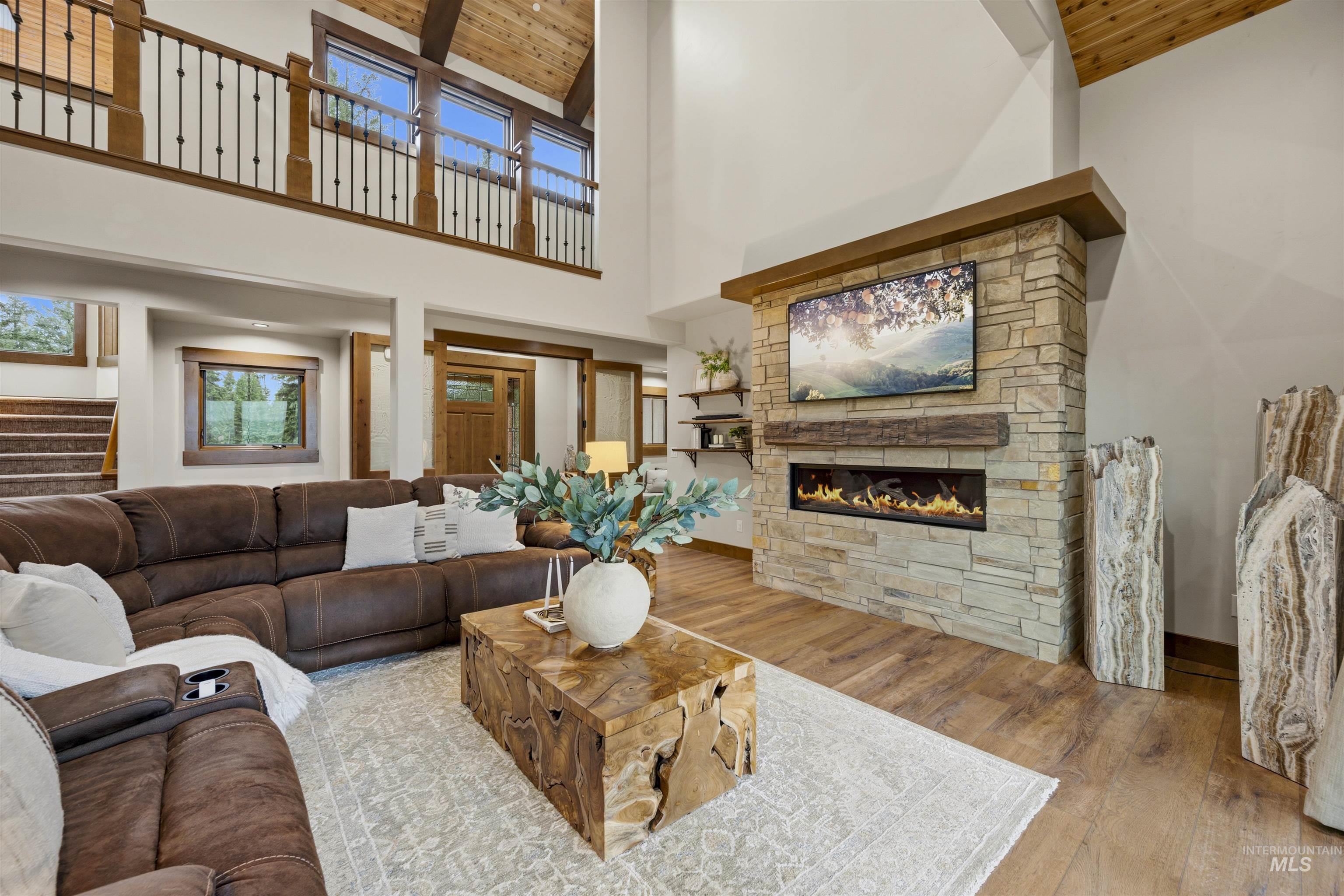Spacious living area featuring a floor-to-ceiling stone fireplace with a linear insert, wood-finish flooring, and a vaulted wood-paneled ceiling