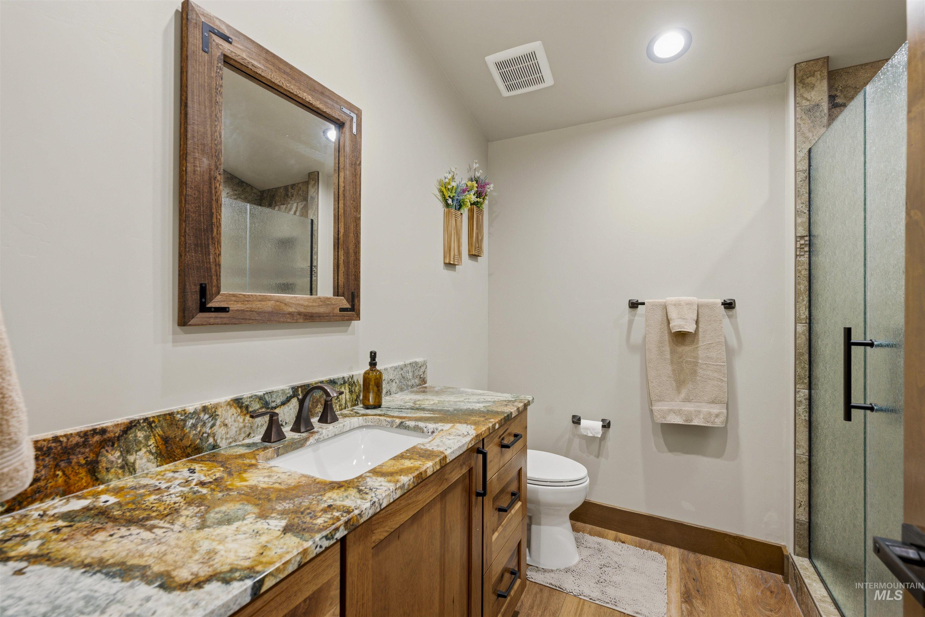 Bathroom featuring a single vanity with an integrated sink, a richly veined stone countertop, and wood-finish cabinetry - Ensuite to Bedroom 3