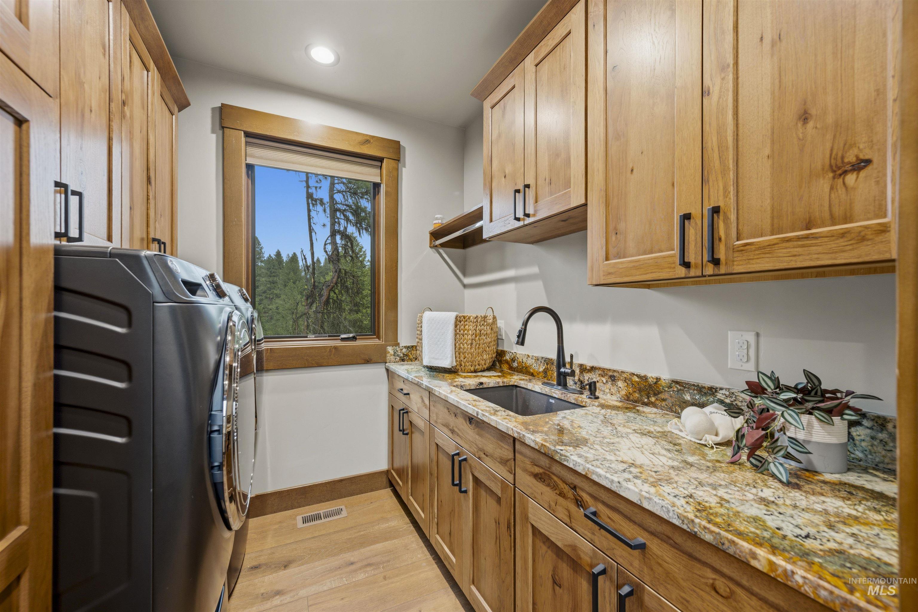 Laundry room featuring light wood-finish cabinetry, granite countertops, a built-in sink with a matte black faucet, and a window with wood trim - Main Level