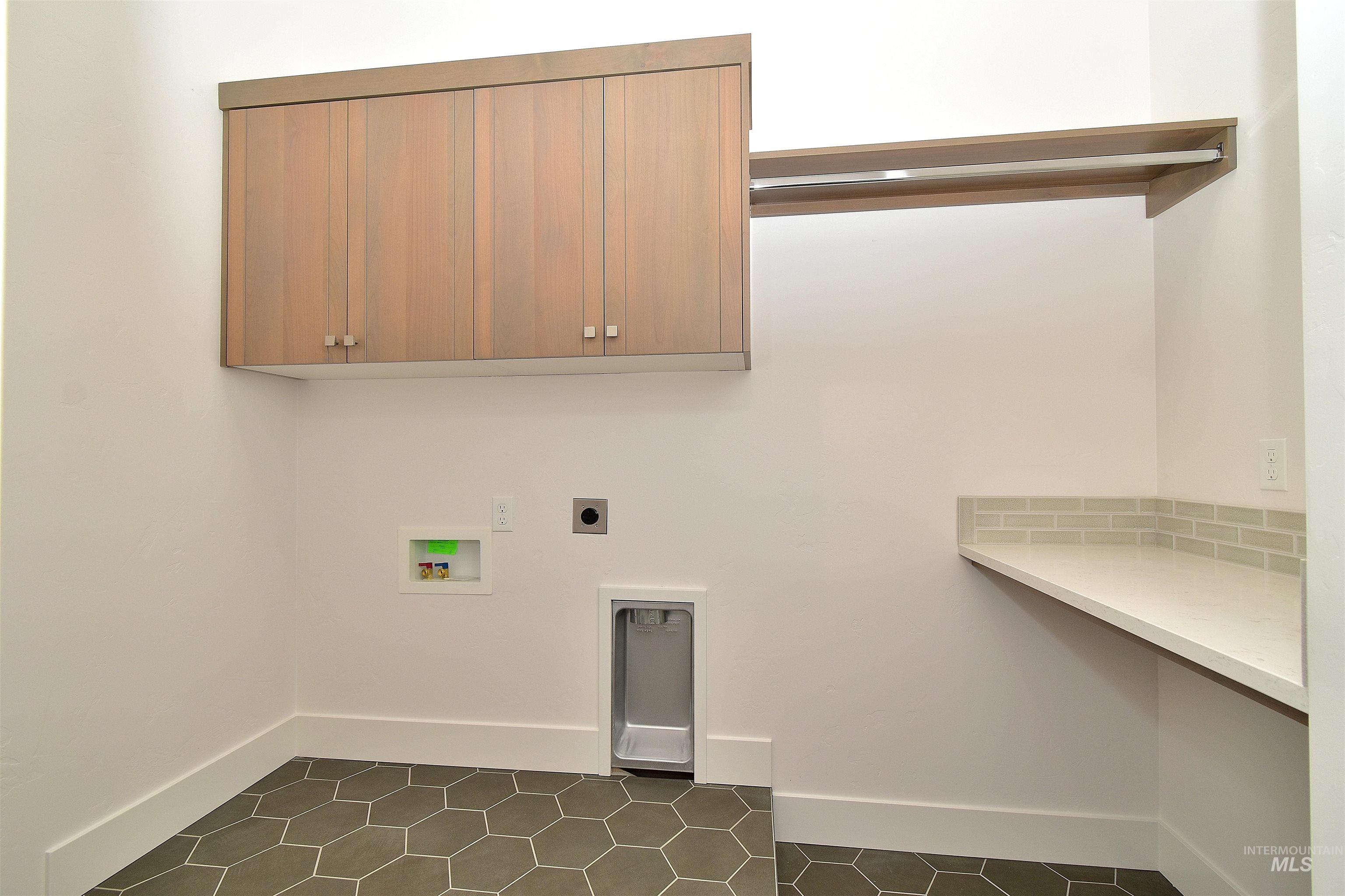 Laundry area with electric dryer hookup, dark tile patterned floors, hookup for a washing machine, and cabinet space