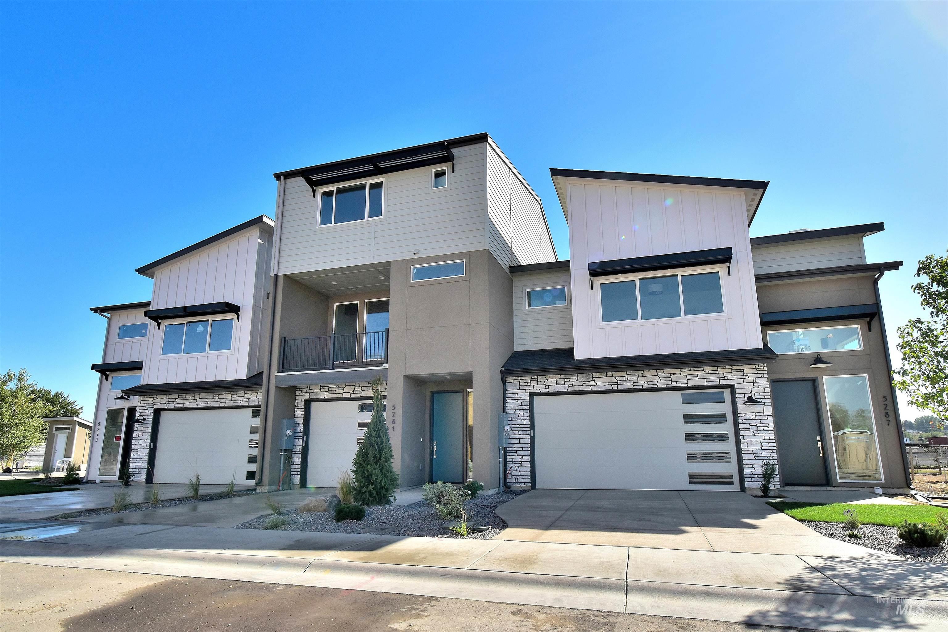Modern home featuring stone siding, a balcony, board and batten siding, concrete driveway, and a garage