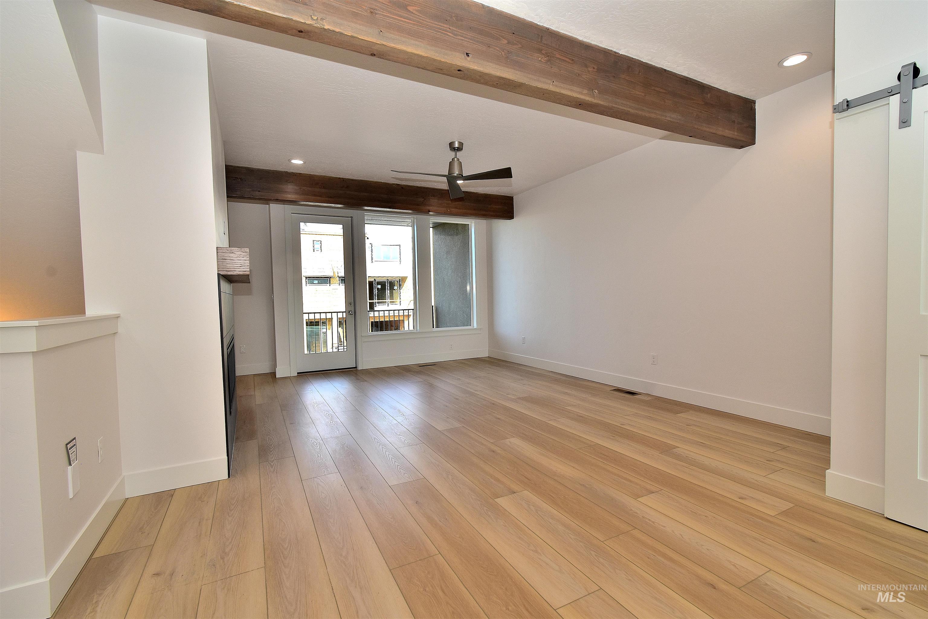 Spare room with a barn door, ceiling fan, beamed ceiling, recessed lighting, and light wood-style floors
