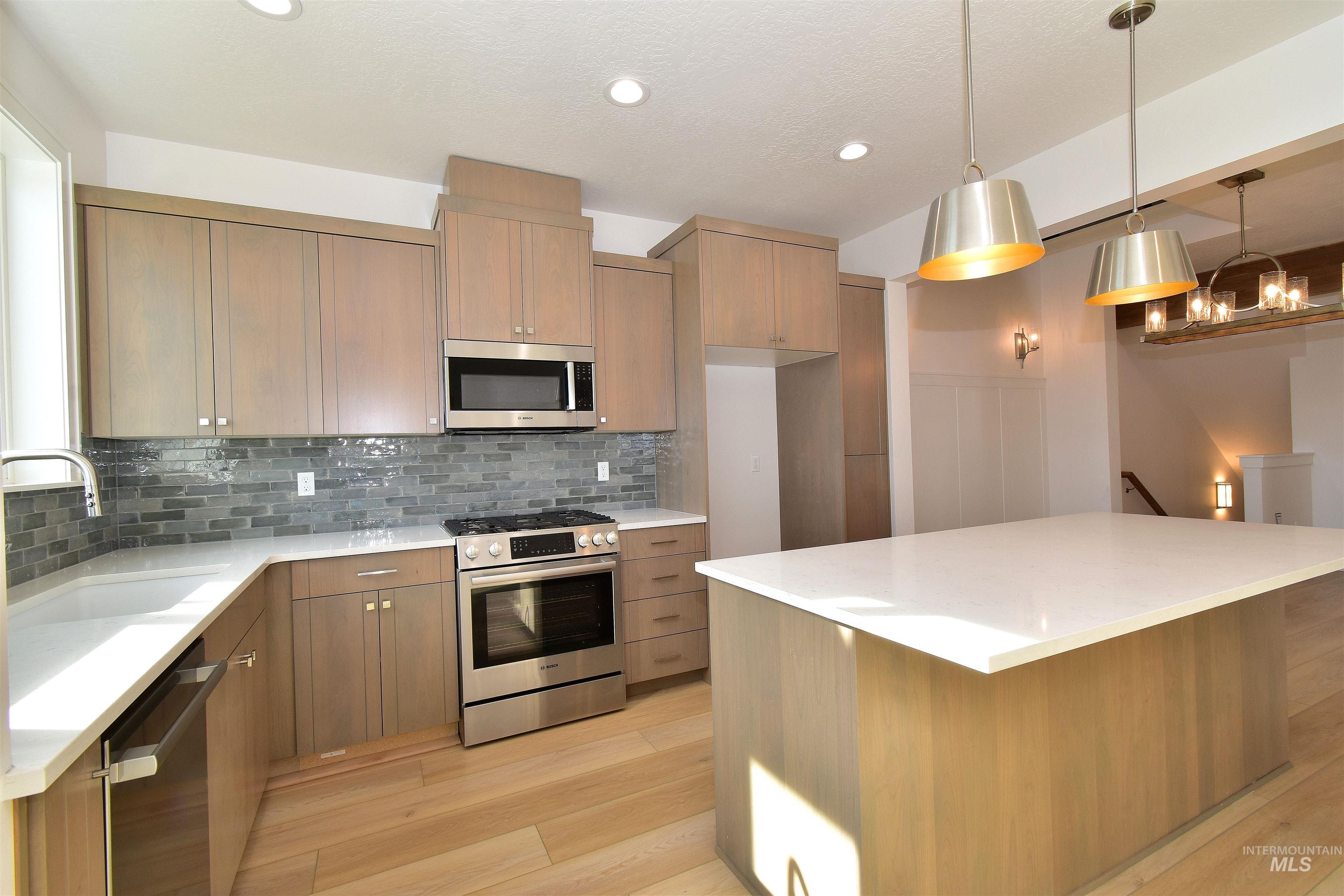 Kitchen featuring stainless steel appliances, light stone countertops, light wood finished floors, a center island, and pendant lighting