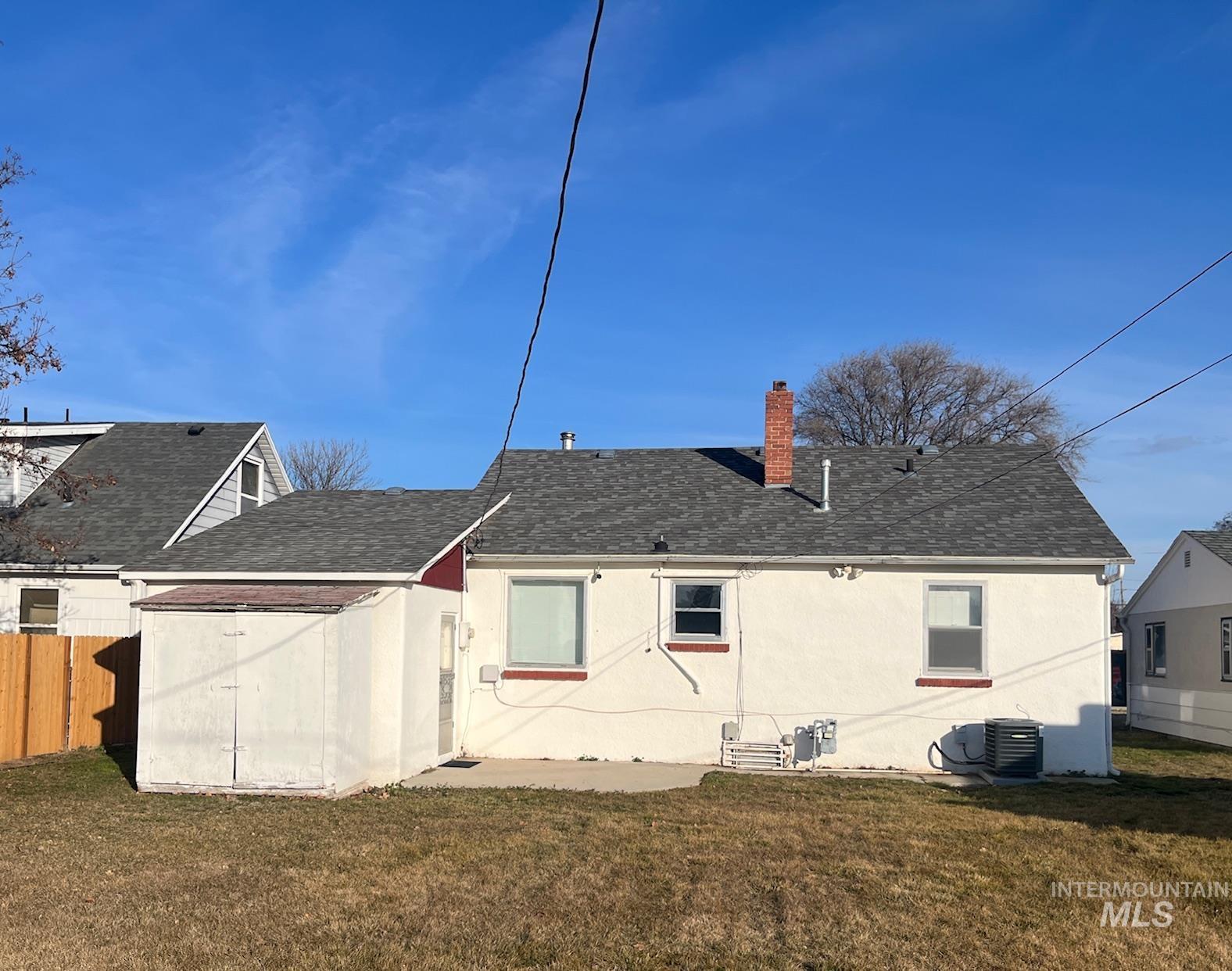 Back of house with a shingled roof, a chimney, stucco siding, and a patio