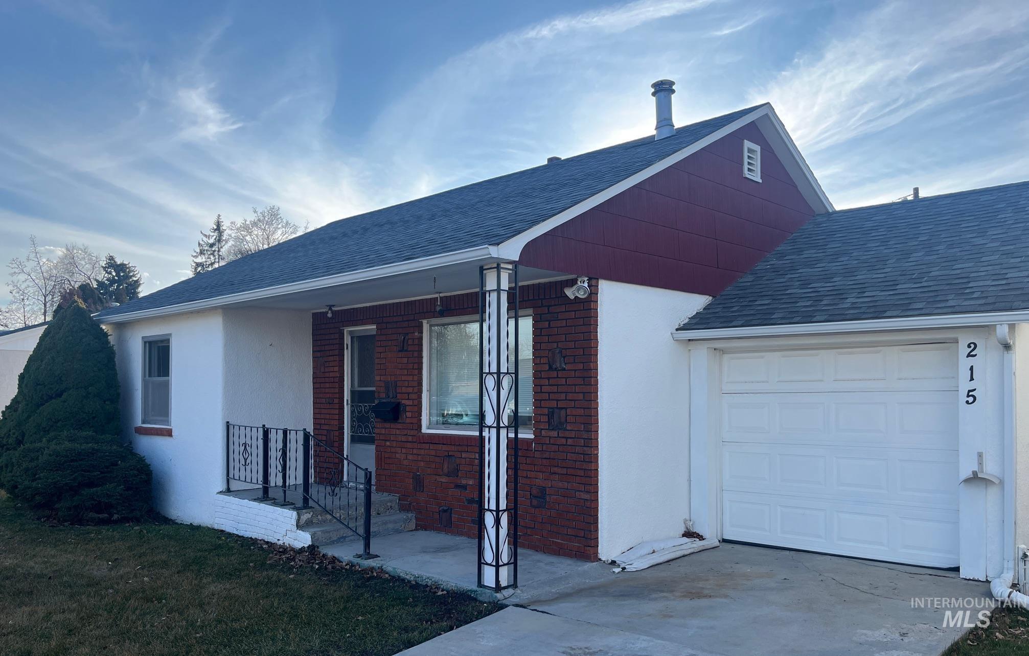 View of front of home with brick siding, roof with shingles, stucco siding, covered porch, and a garage