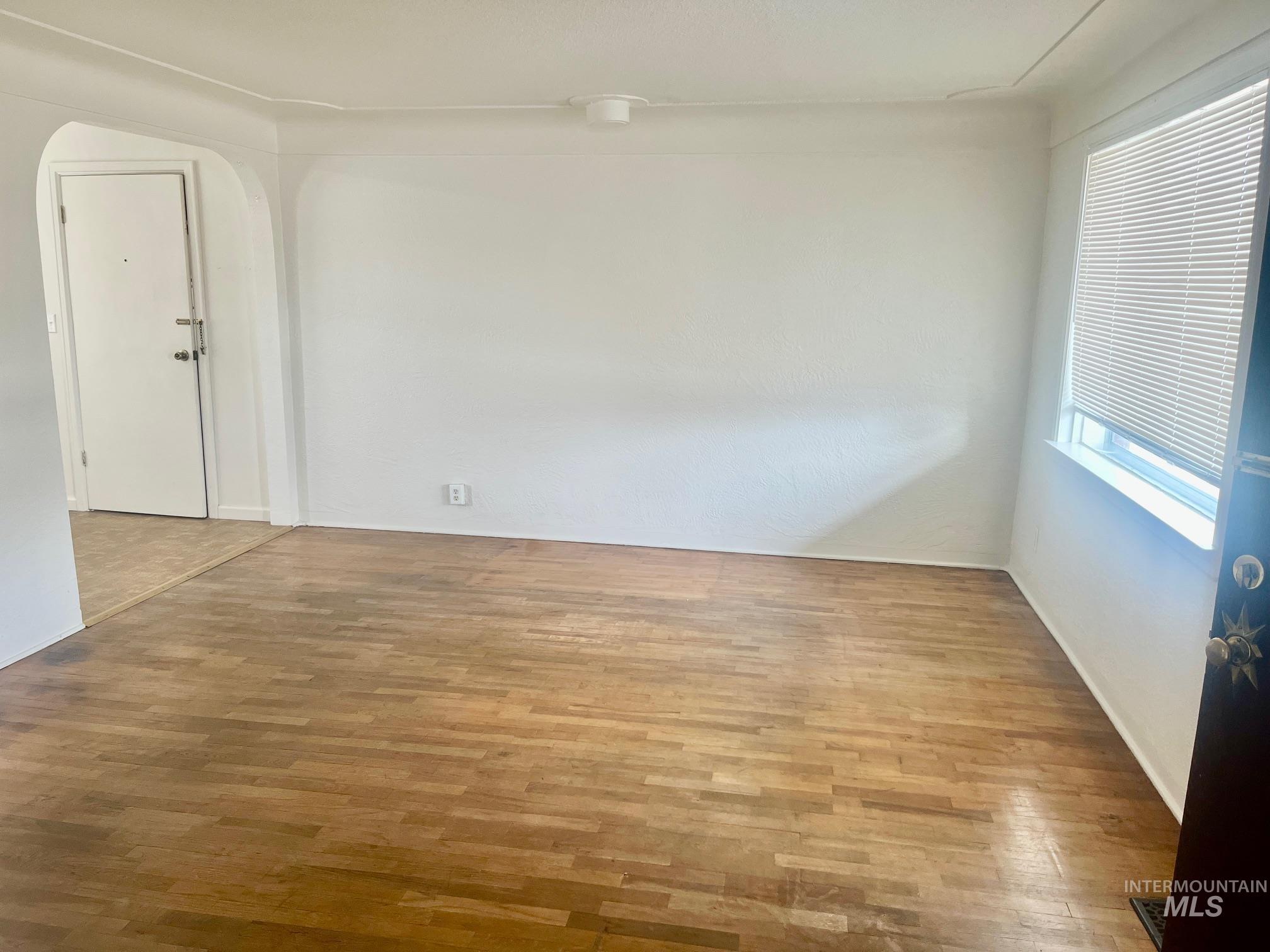 Unfurnished room featuring arched walkways and wood finished floors