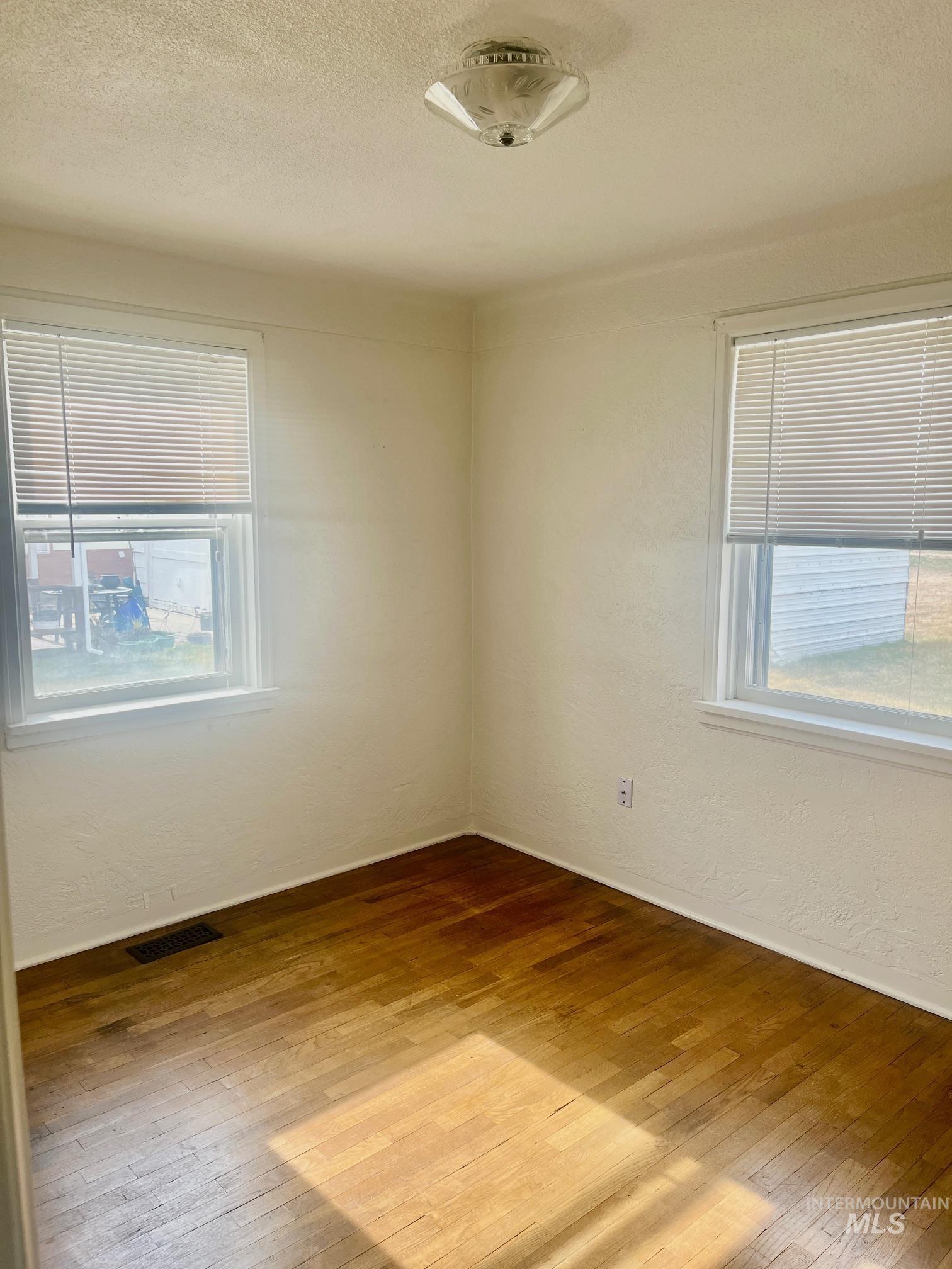Unfurnished room with a textured wall, a textured ceiling, and light wood-type flooring