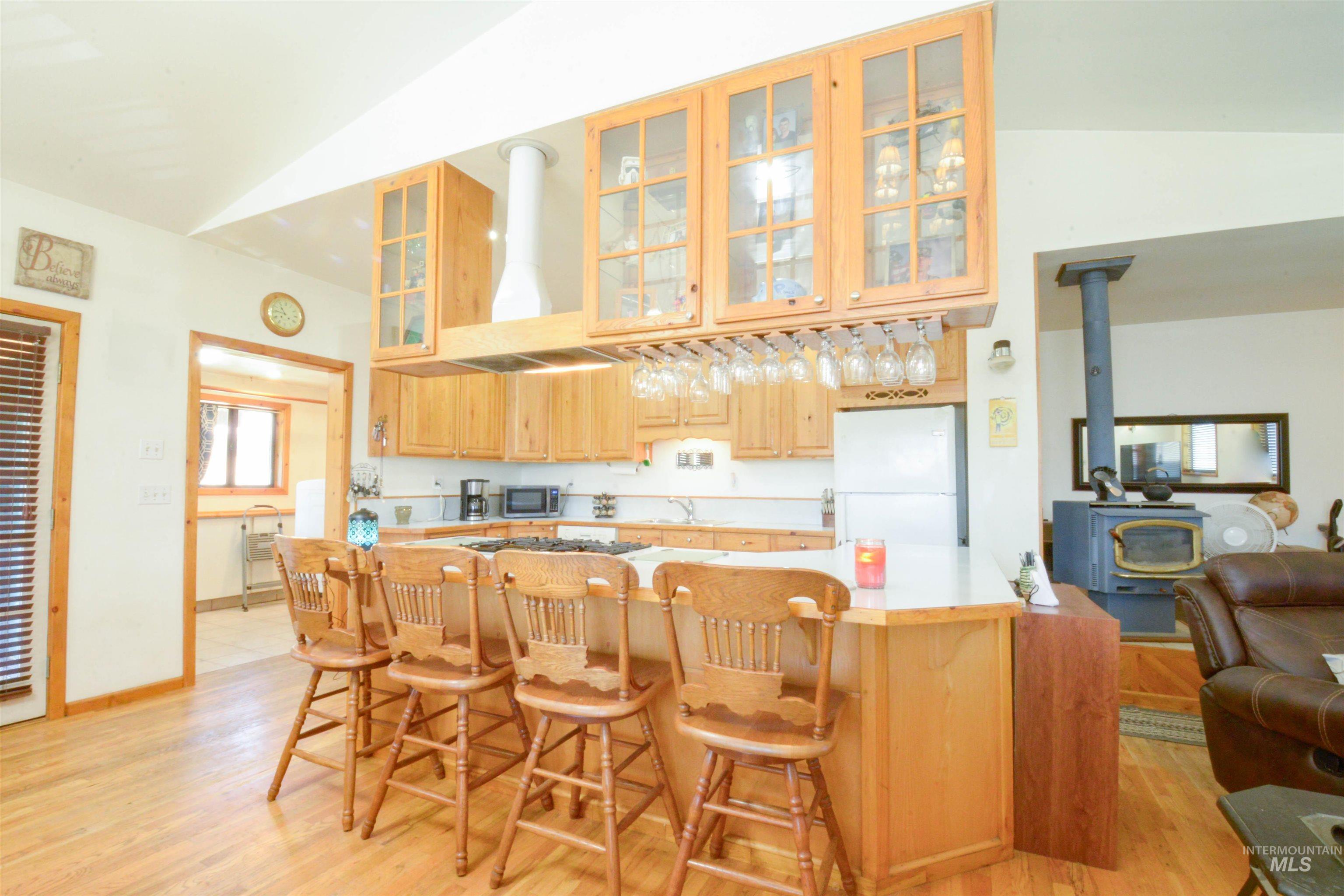 Kitchen featuring a wood stove, freestanding refrigerator, light wood-style floors, light brown cabinets, and lofted ceiling