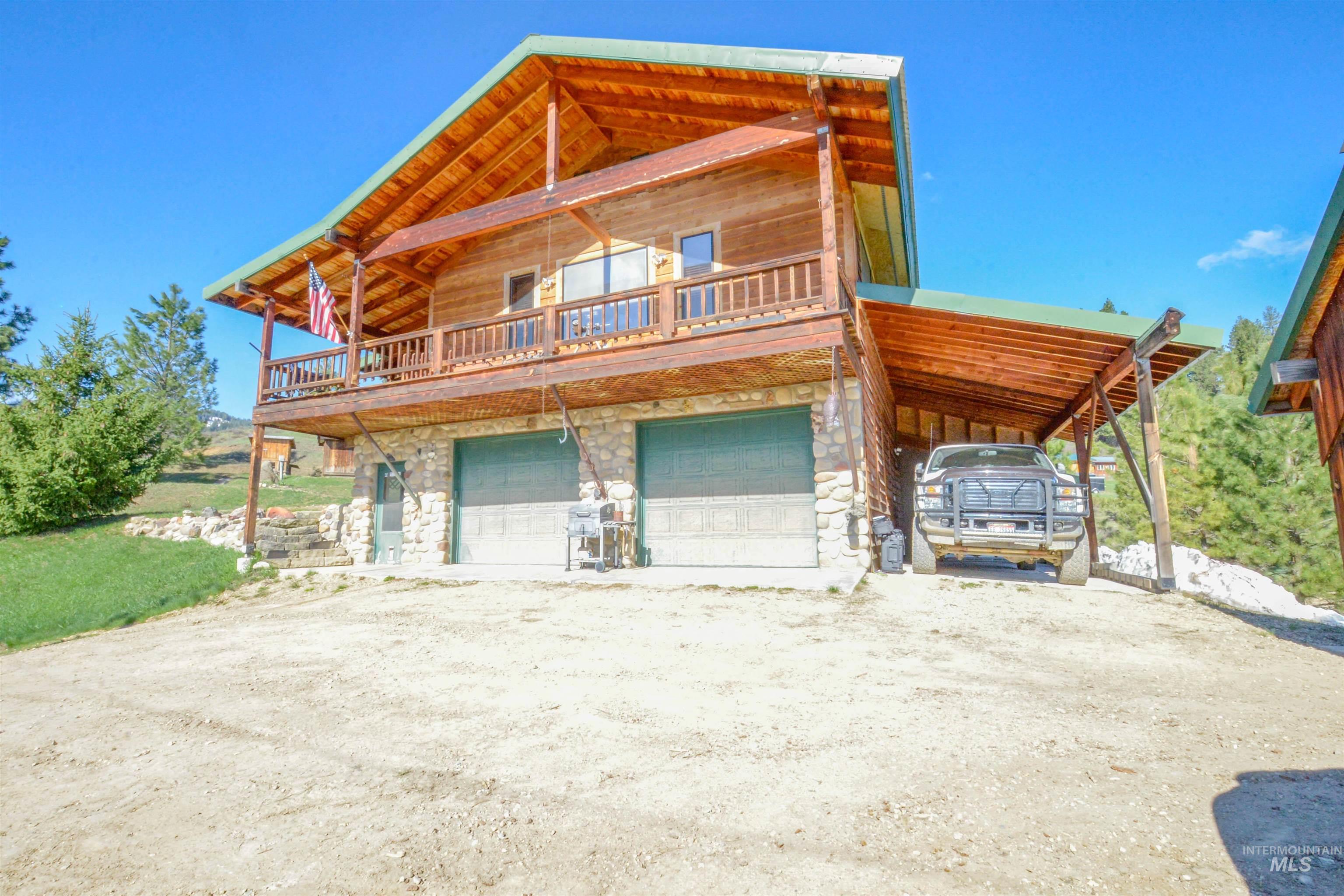Log-style house with stone siding, a carport, dirt driveway, and a garage