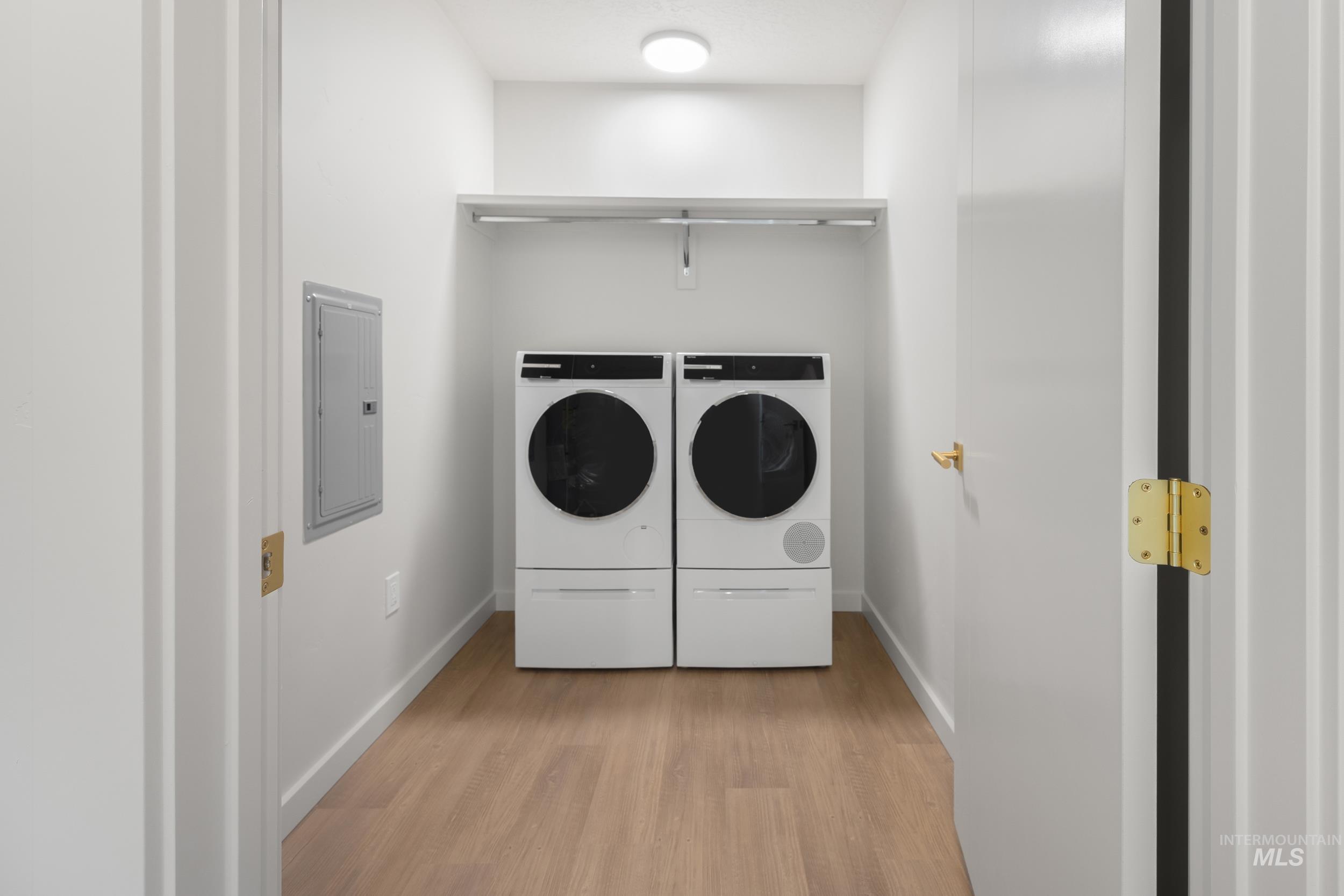 Laundry room featuring light wood-style flooring, electric panel, and separate washer and dryer